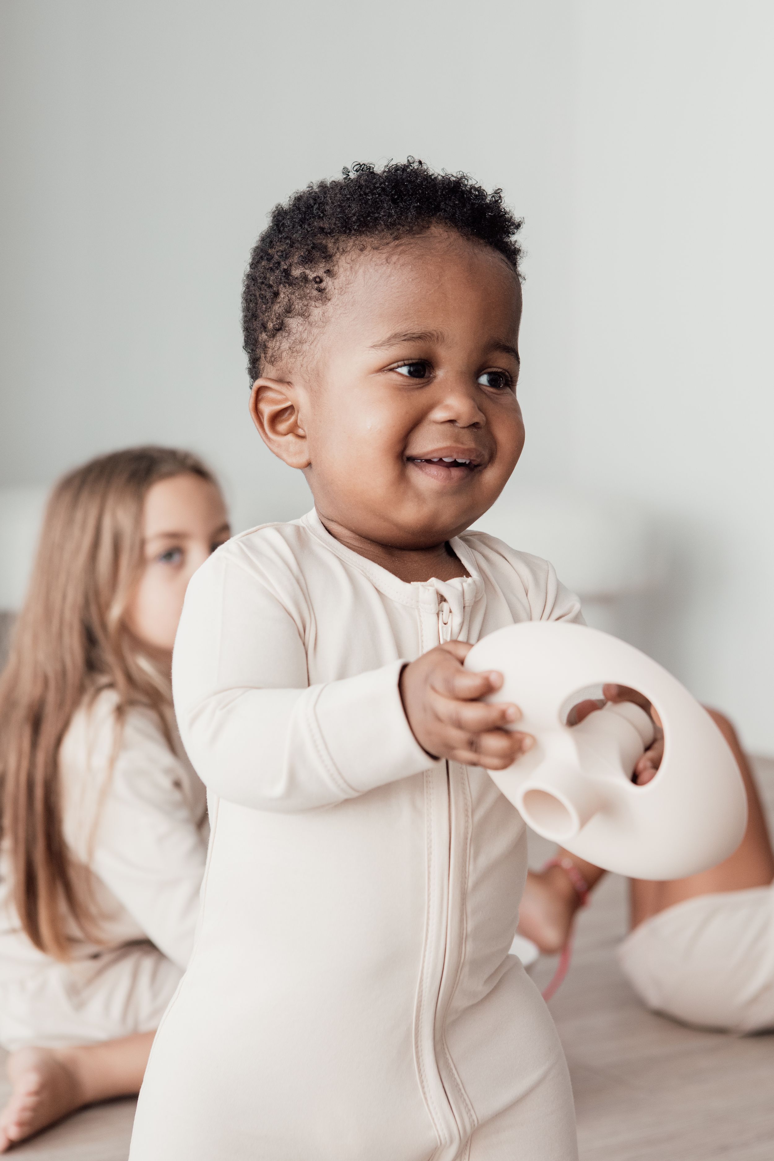Young toddler in cream-colored zippered pajamas playing with a white object.