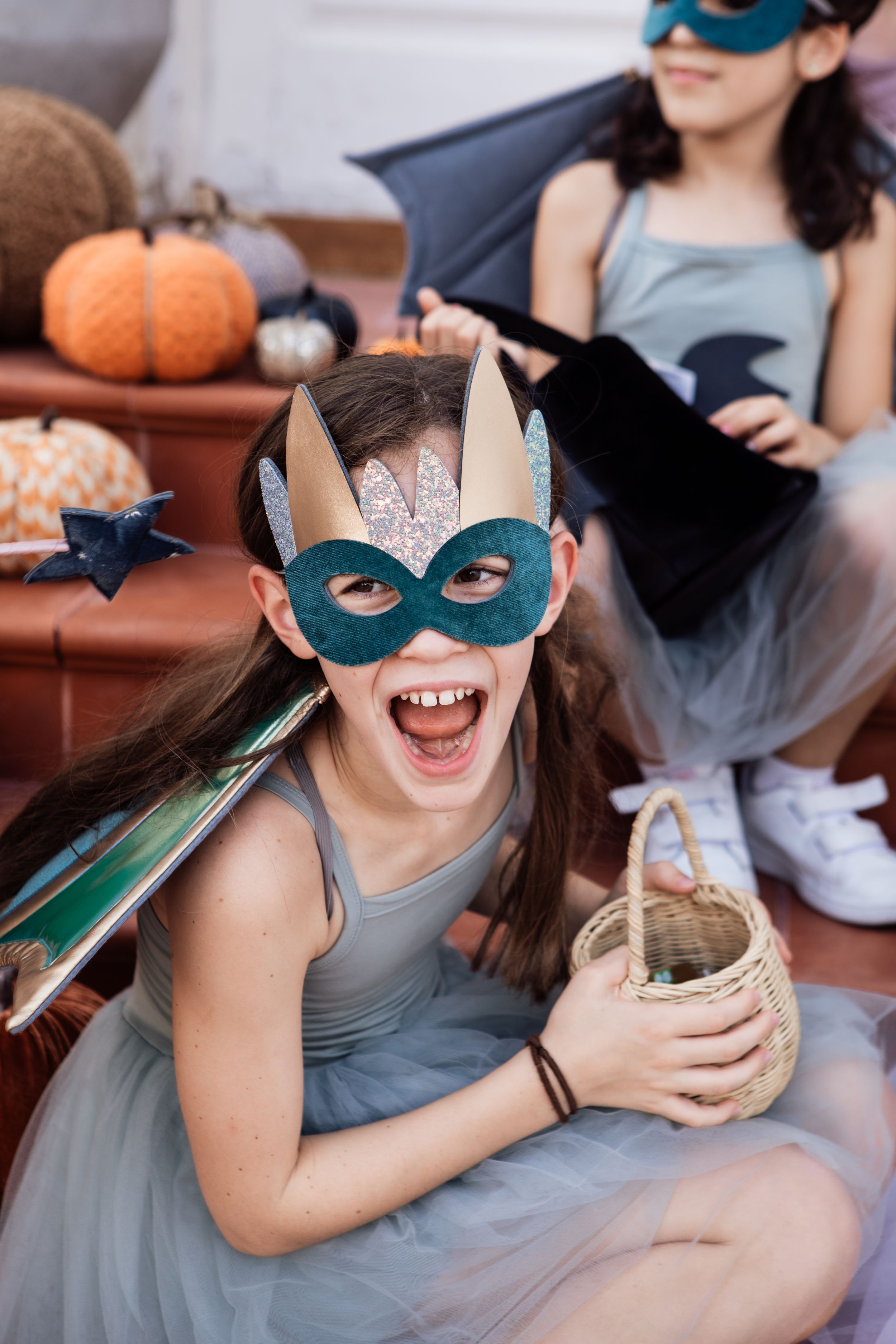 Festive Halloween scene with someone wearing a teal mask and holding a basket near pumpkin decorations.