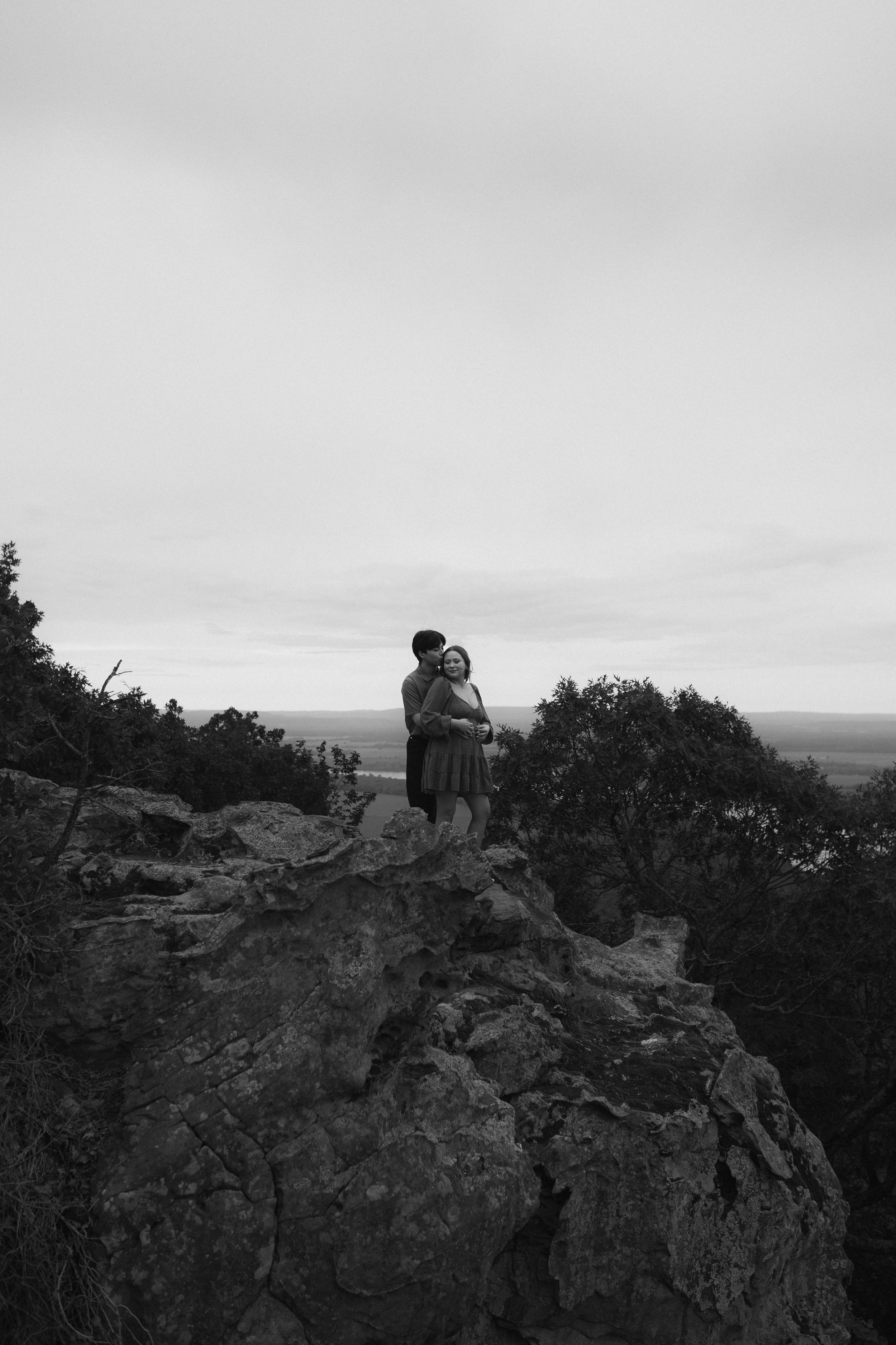 Black and white landscape photo of figures sitting on rocky cliffs overlooking a valley.