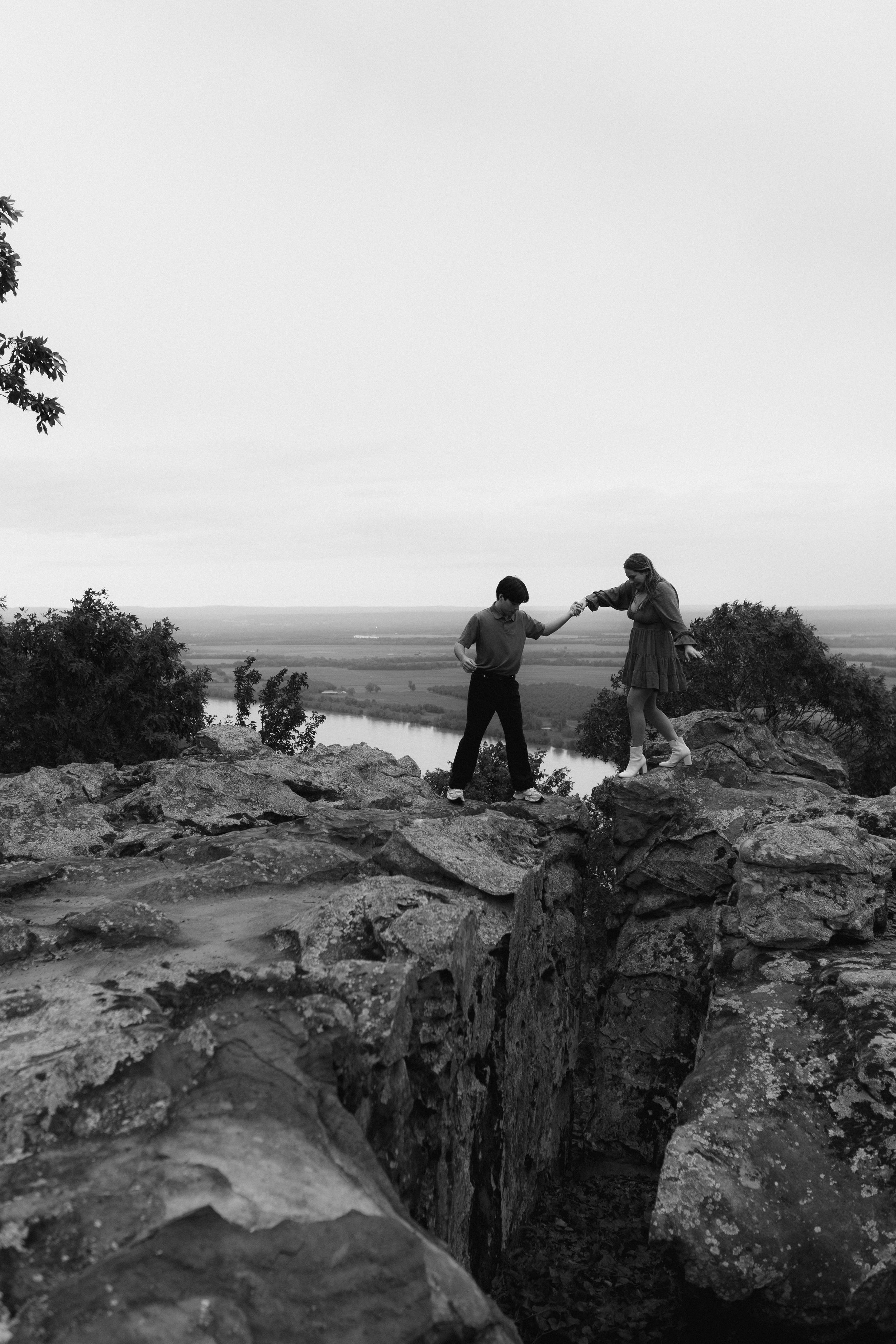 Couple exploring rocky cliffs during an outdoor photoshoot with scenic valley views.