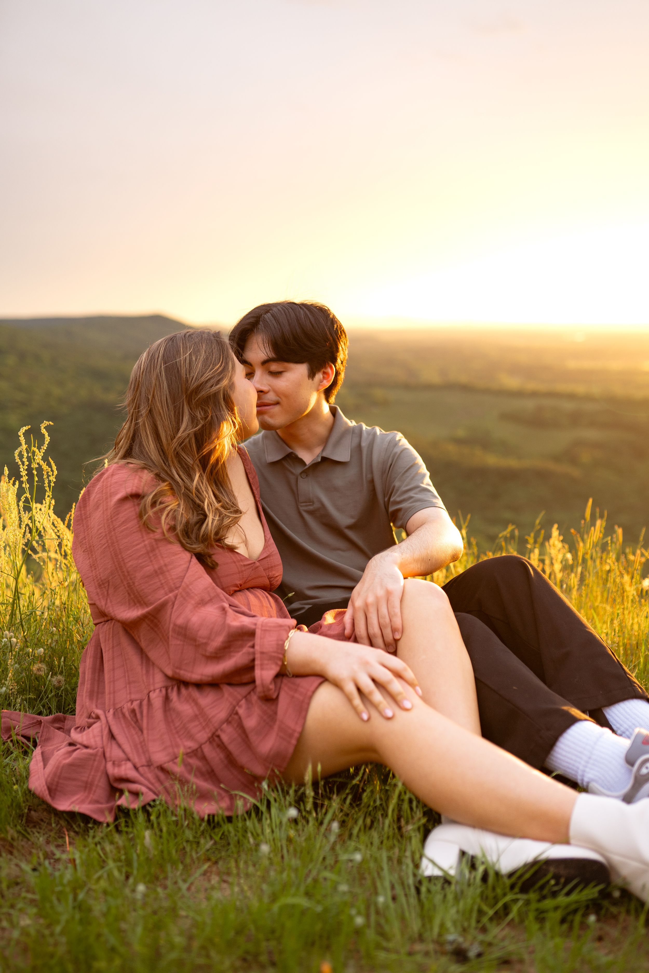 Couple lounging in golden sunset light among wildflowers on hilltop.
