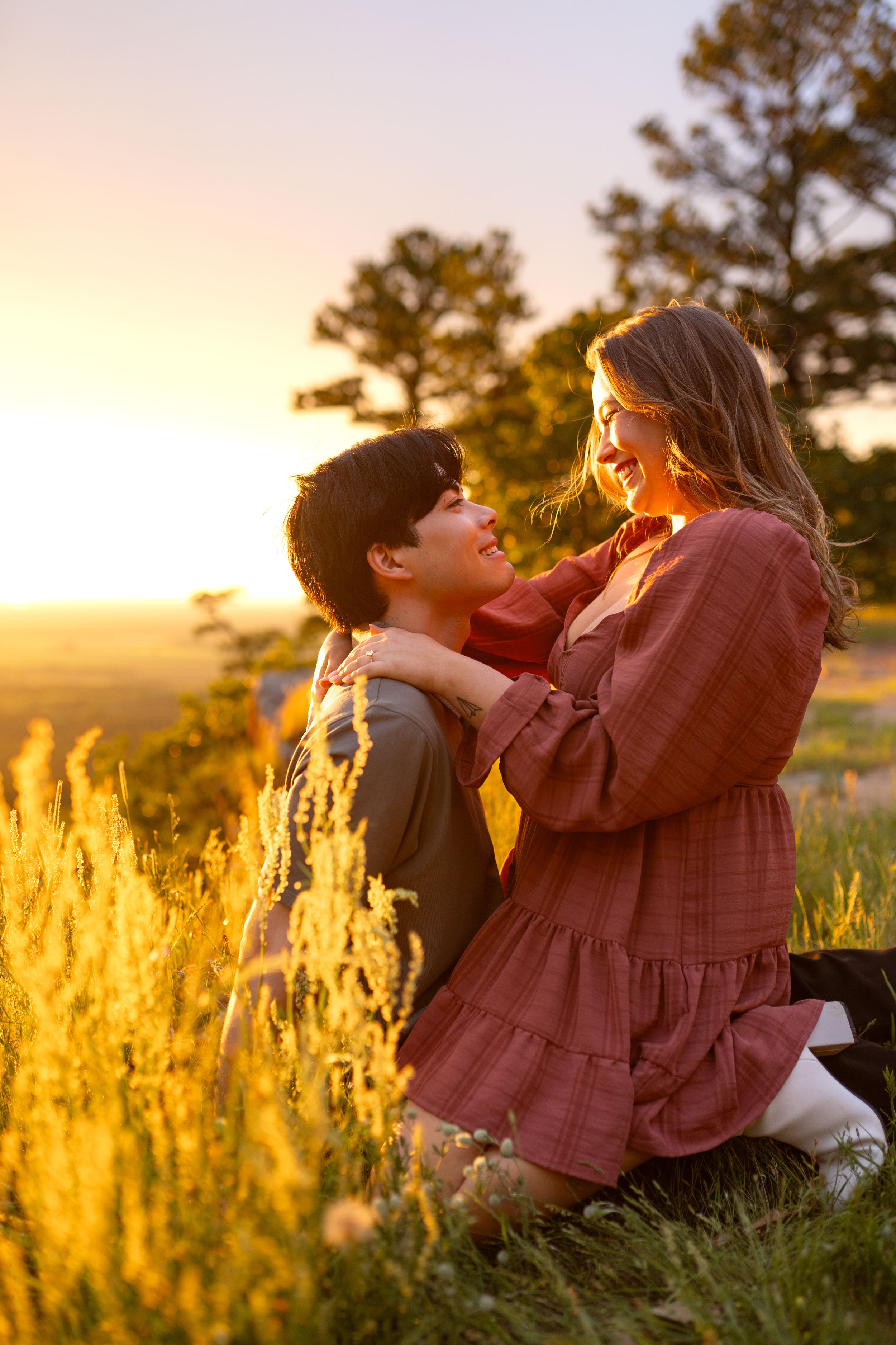 Two people embracing on a hilltop during golden hour with tall grass swaying in the breeze.