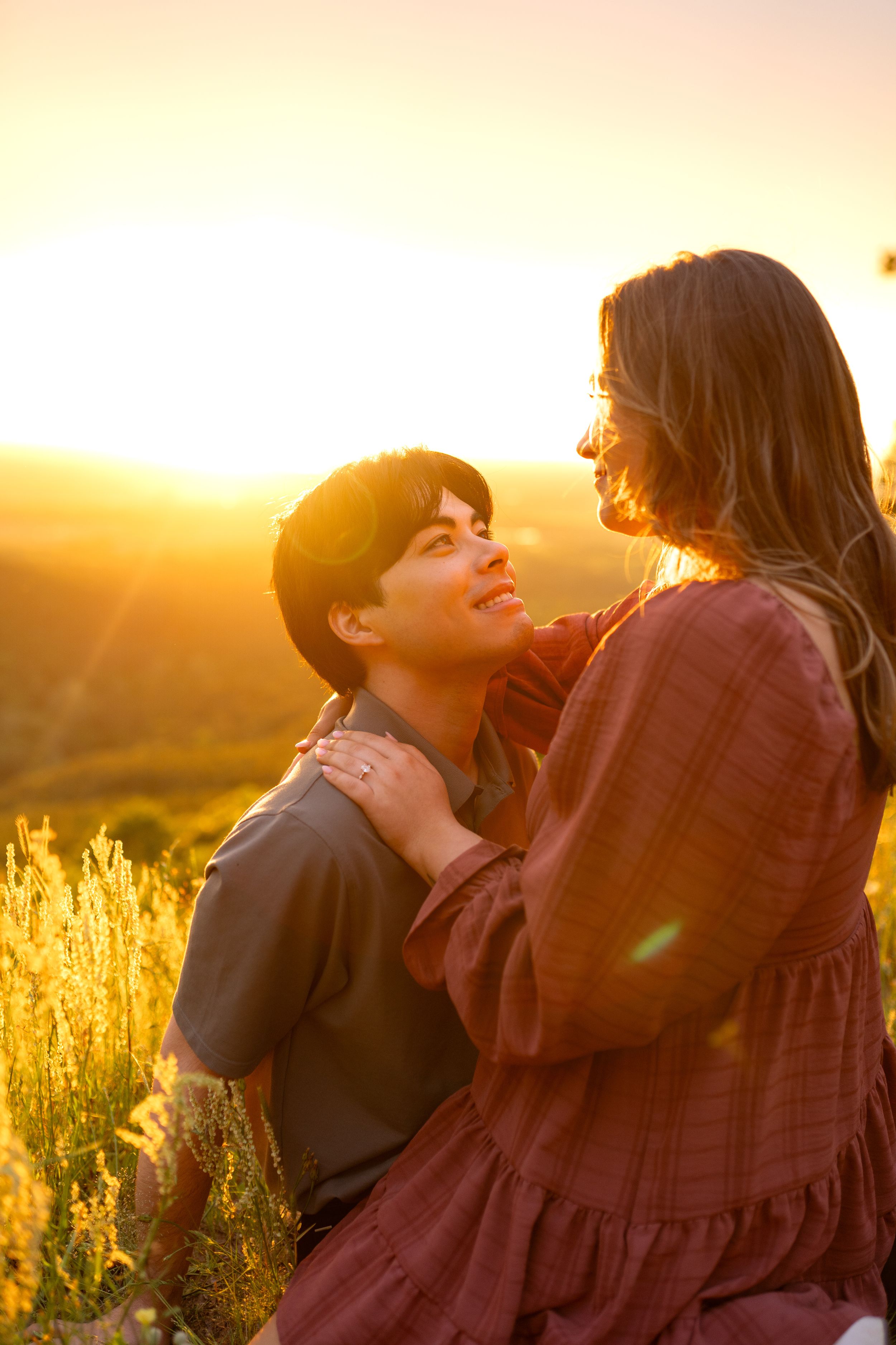Romantic couple laughing together in a sunlit field during sunset.