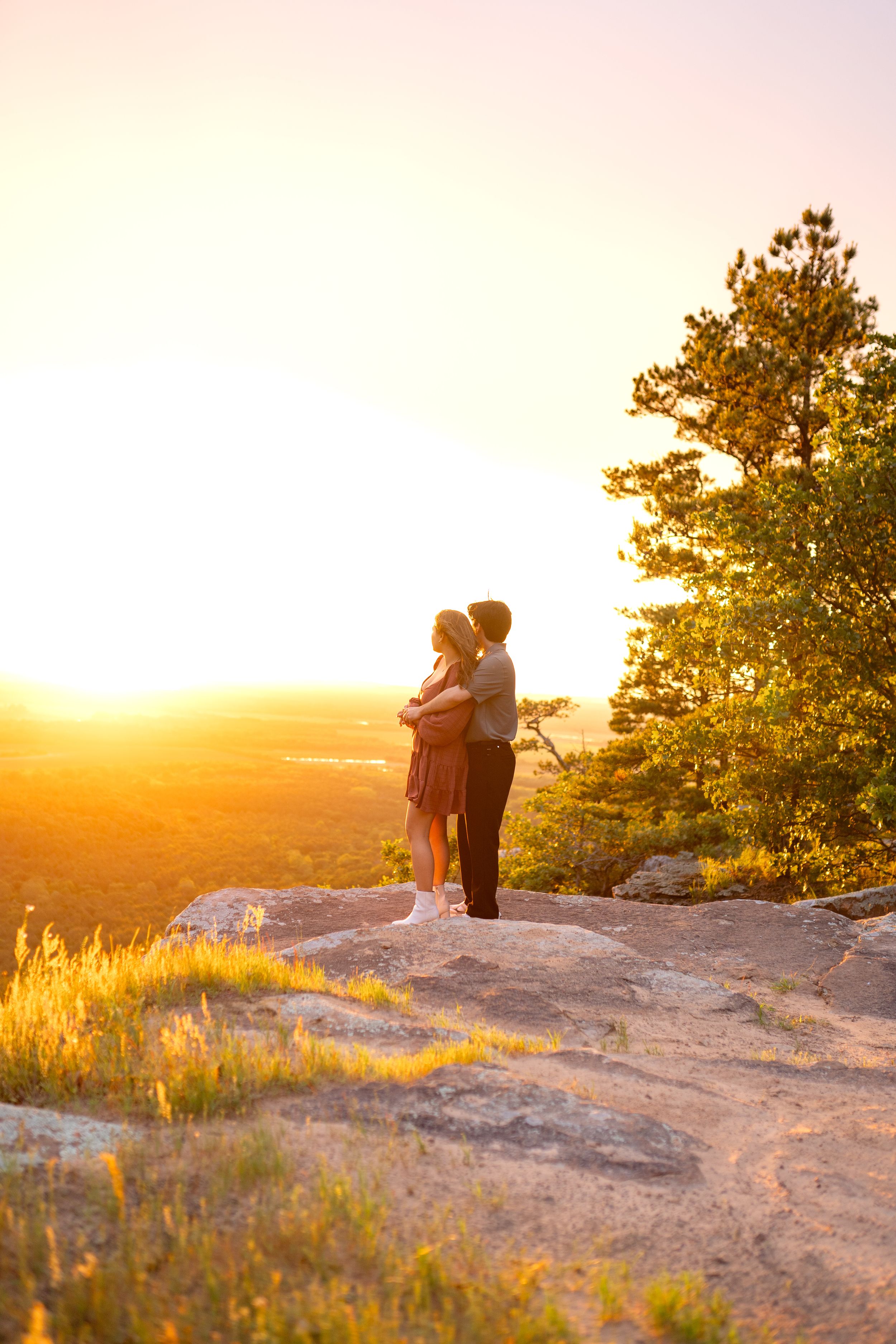 Two people sharing a tender moment on rocky overlook during golden hour.