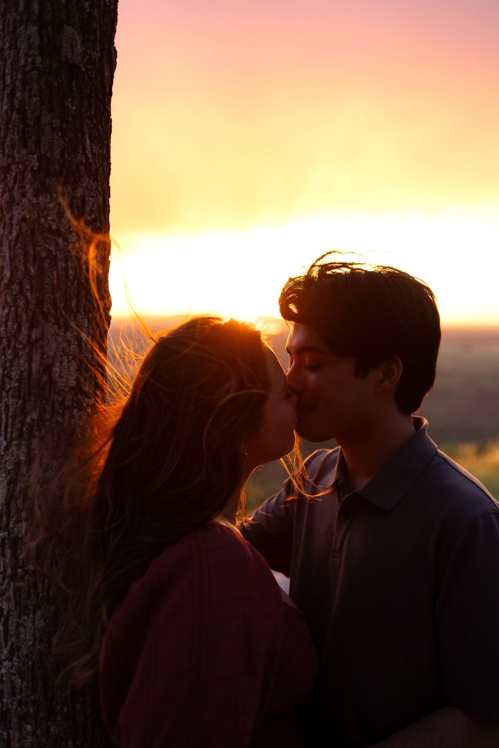 Intimate moment shared between two people beneath a tree at sunset.