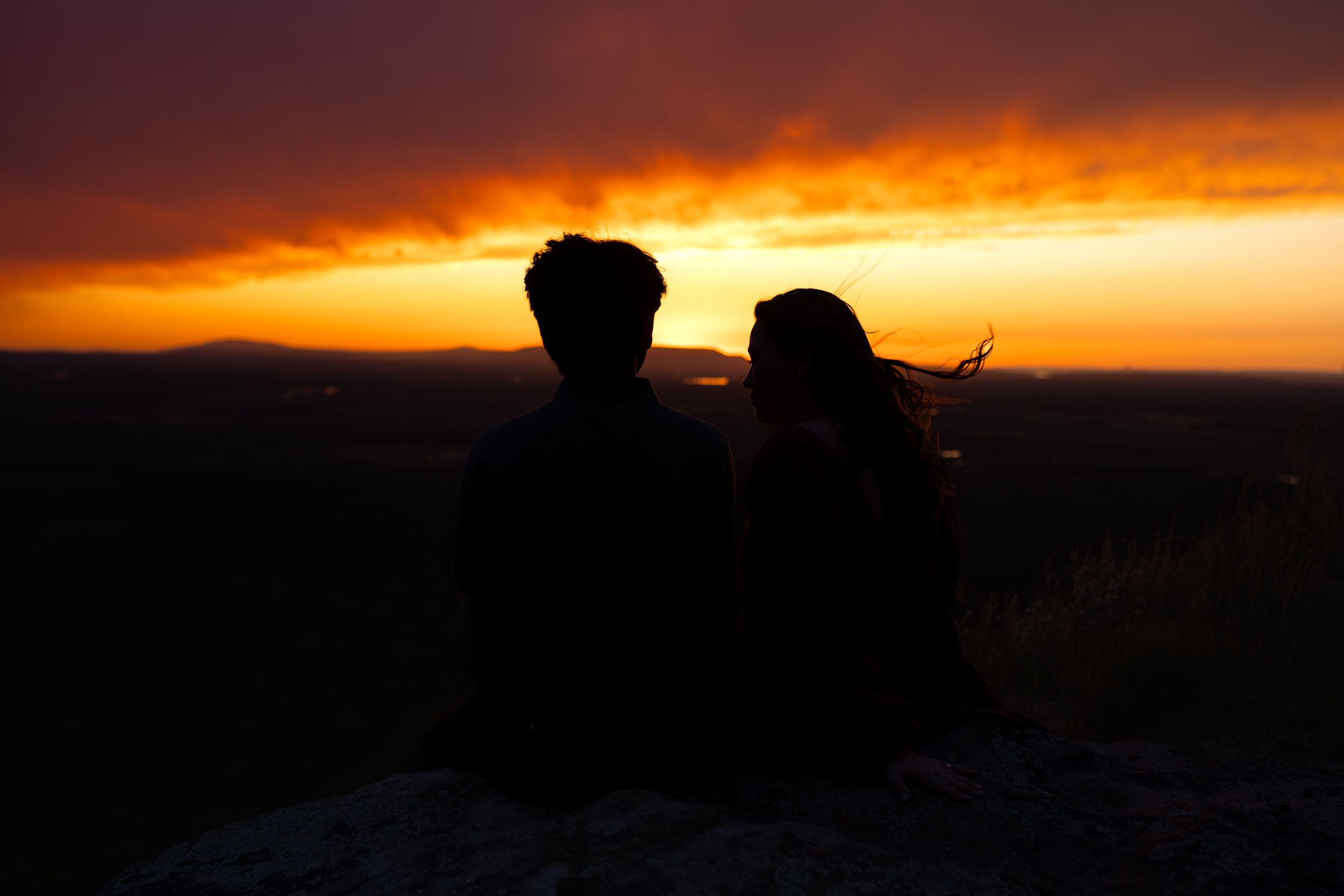 A couple shares an intimate moment silhouetted against a vibrant orange sunset sky.