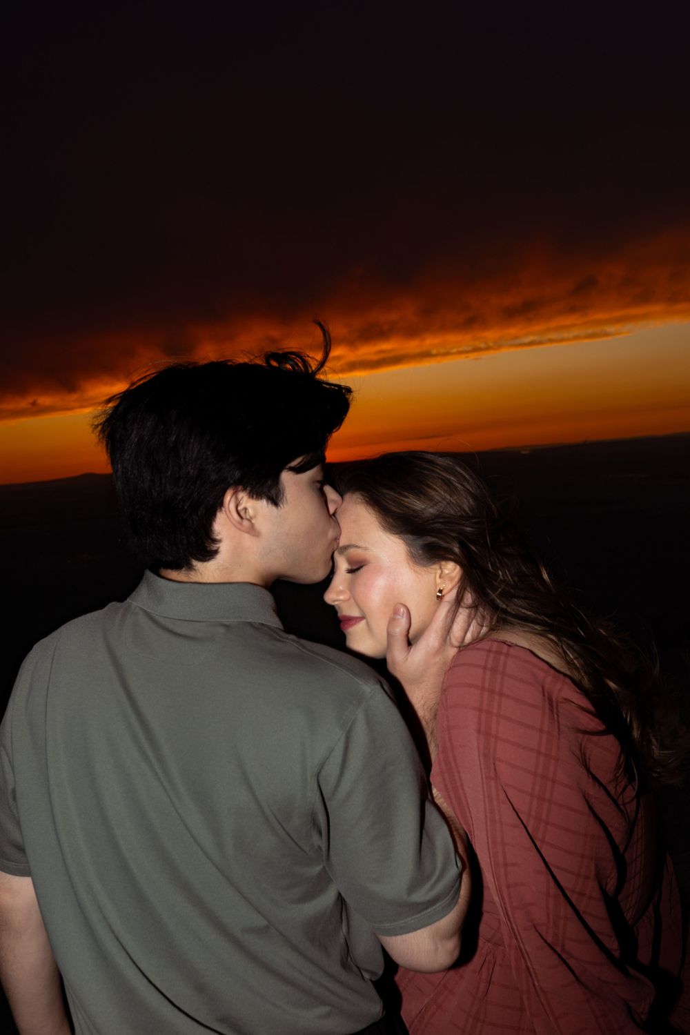 Two figures embrace during golden hour with a dramatic sunset backdrop.