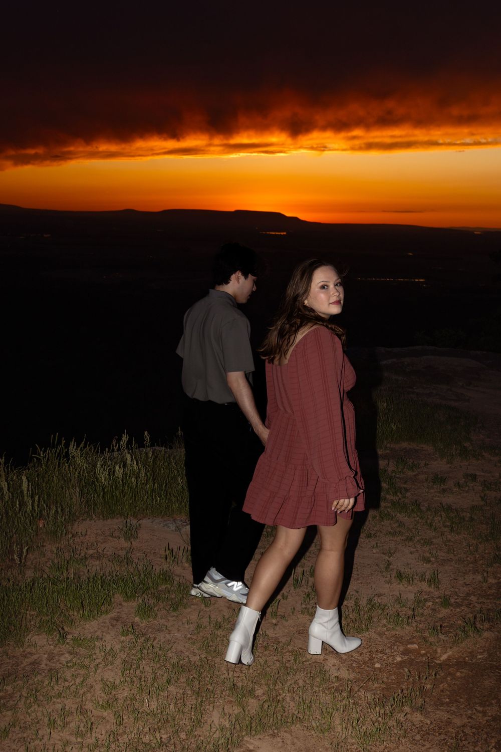 A couple stands together on a grassy hill during a beautiful sunset.