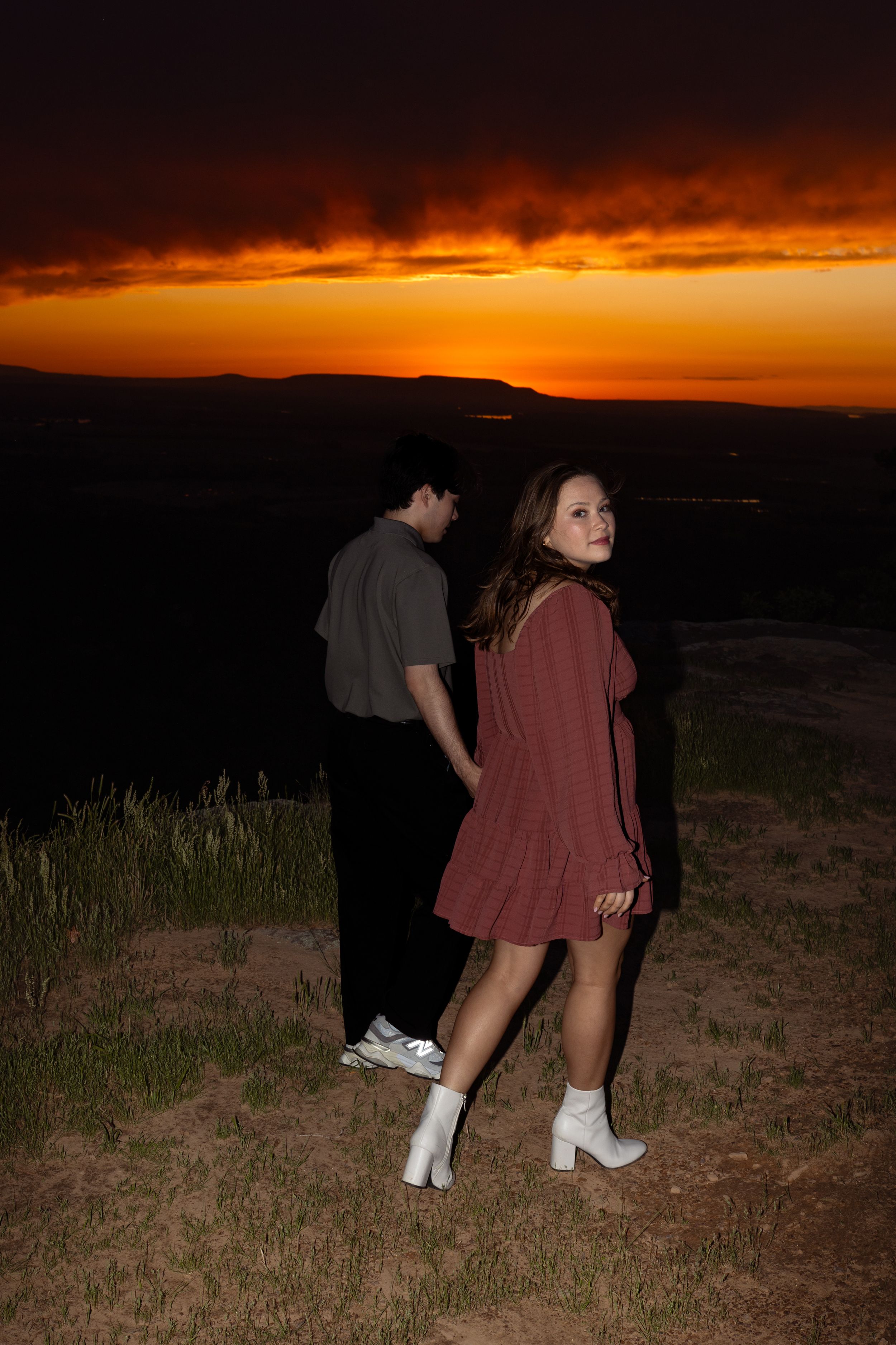 A couple stands together on a grassy hill during a beautiful sunset.