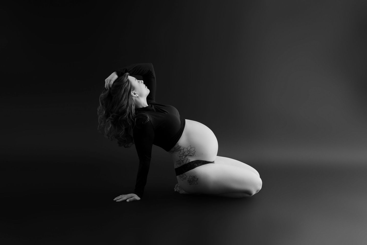 Artistic black and white maternity photo on dark background.