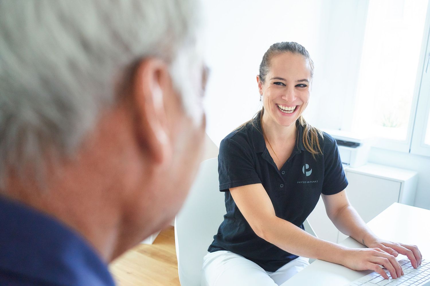 Smiling female healthcare professional consulting with an elderly patient at a desk.