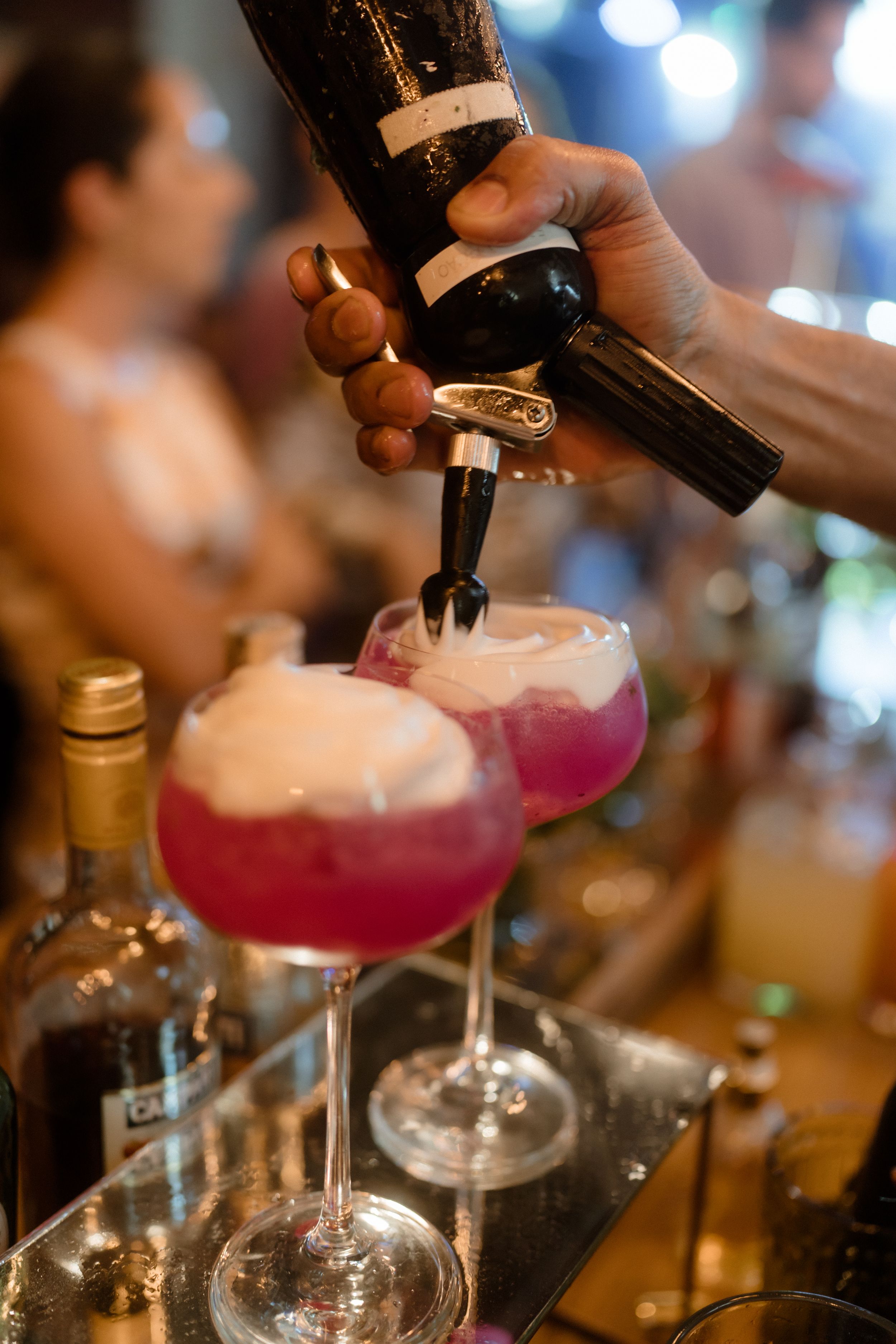 Bartender pouring pink cocktails into glasses at a bar.
