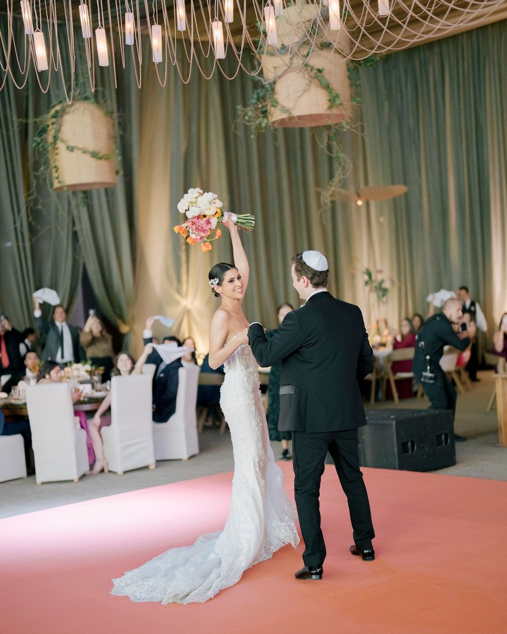 A couple dances gracefully on a pink carpeted floor at an elegant wedding reception with teal curtains.