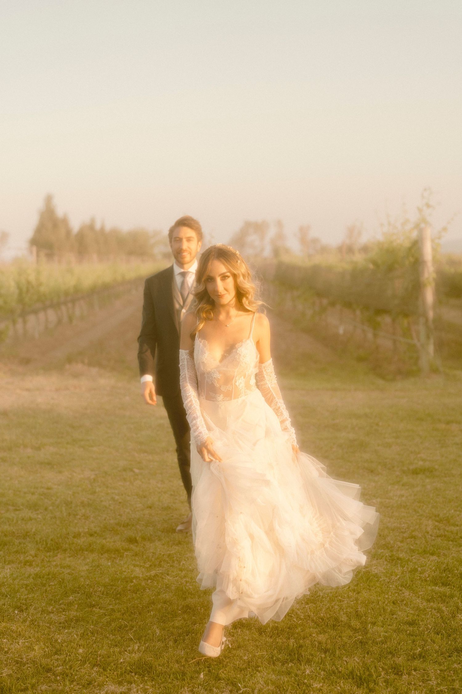 Dreamy golden hour sequence of couple walking through a vineyard in formal wedding attire.
