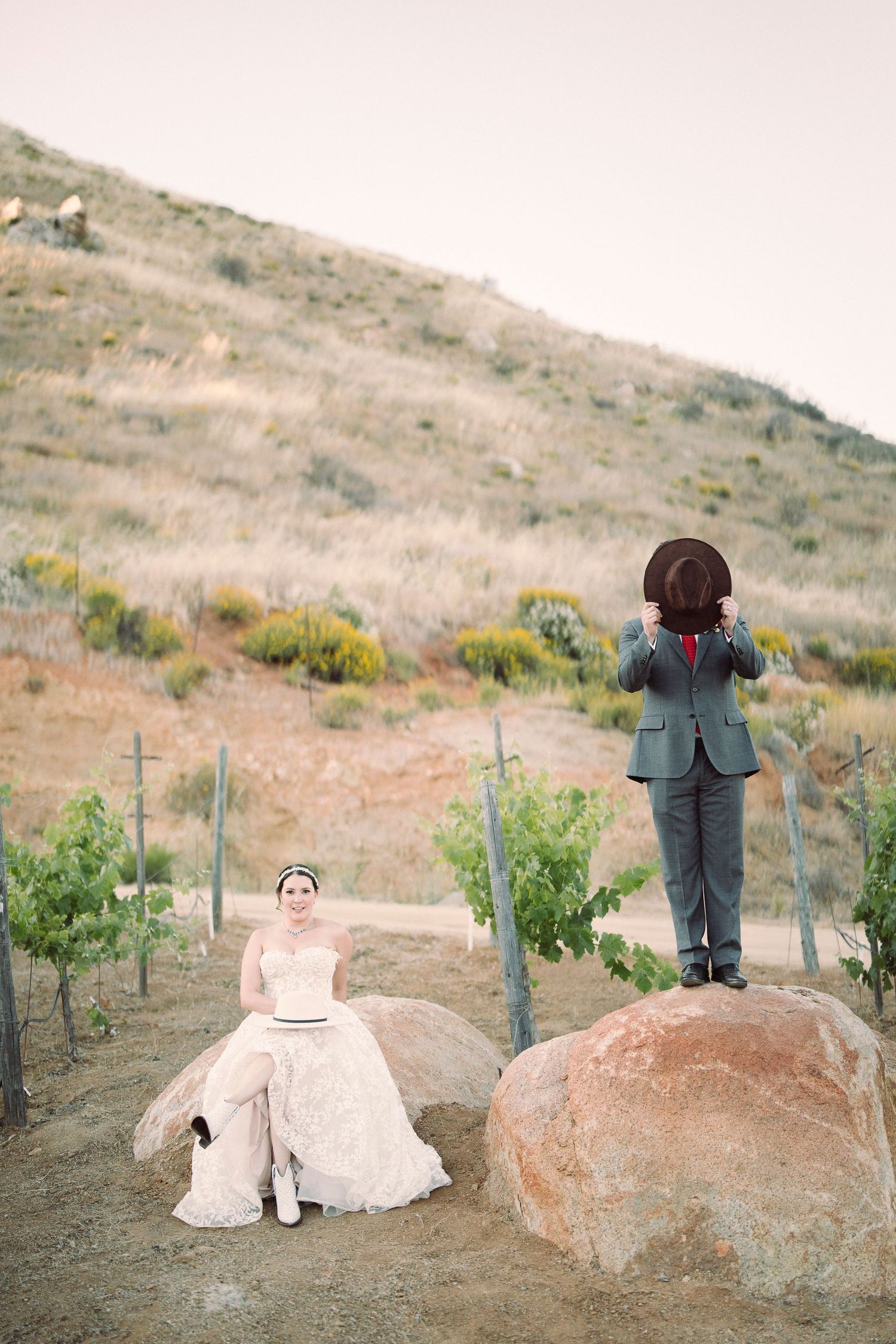 Creative wedding photography sequence of a couple sitting on large rocks in a hillside vineyard.