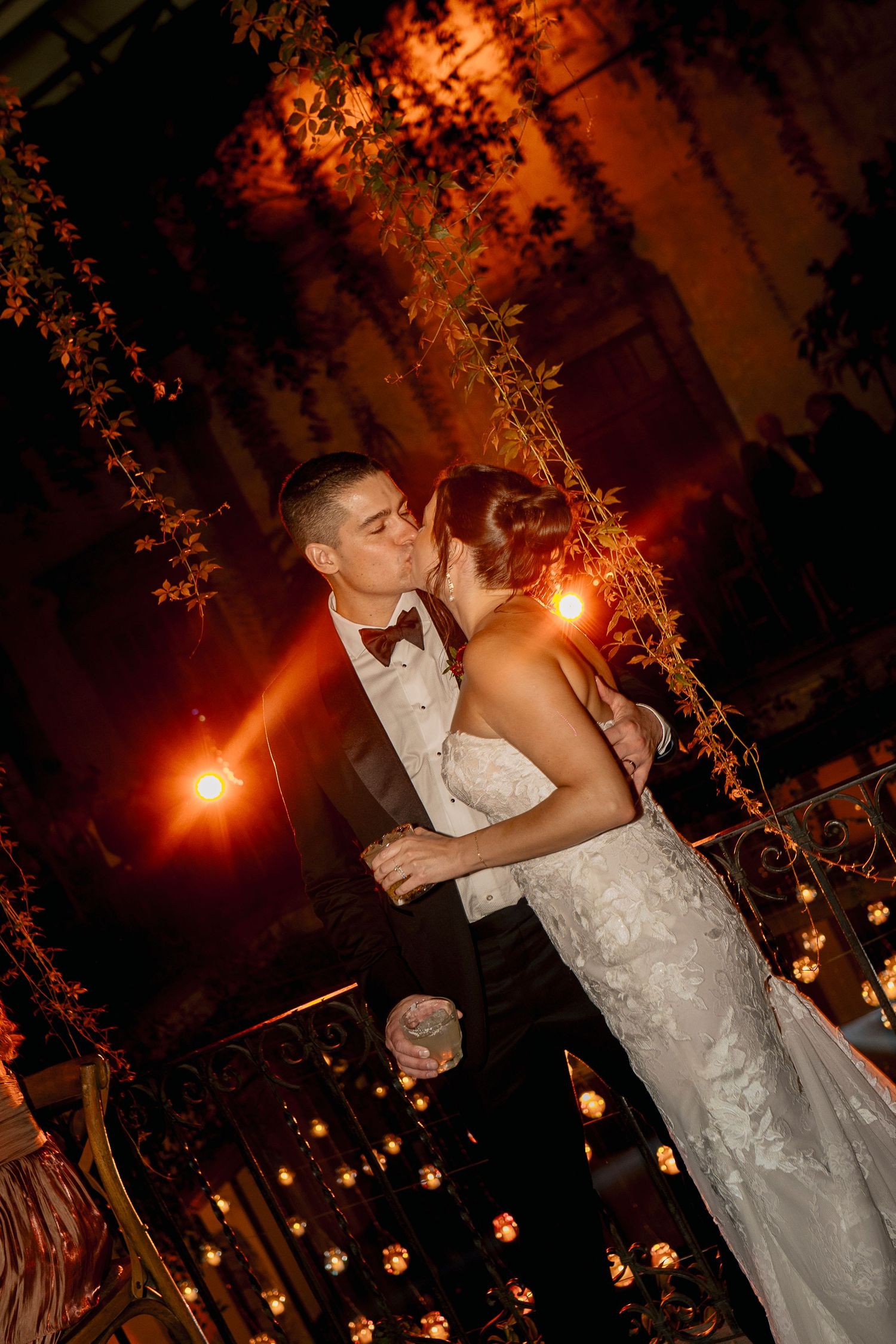 A couple shares a romantic dance at a nighttime wedding reception under glowing string lights and floral decor.
