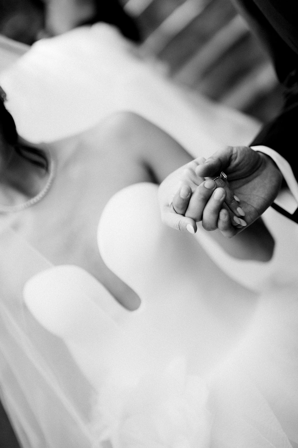 A tender black and white image of two hands gently clasped together with soft fabric in the background.