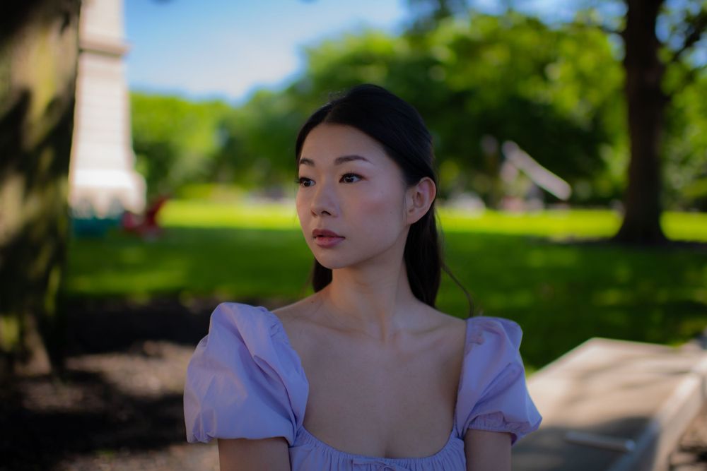 Summer portrait outdoors featuring a purple dress with puff sleeves against a blurred green background.