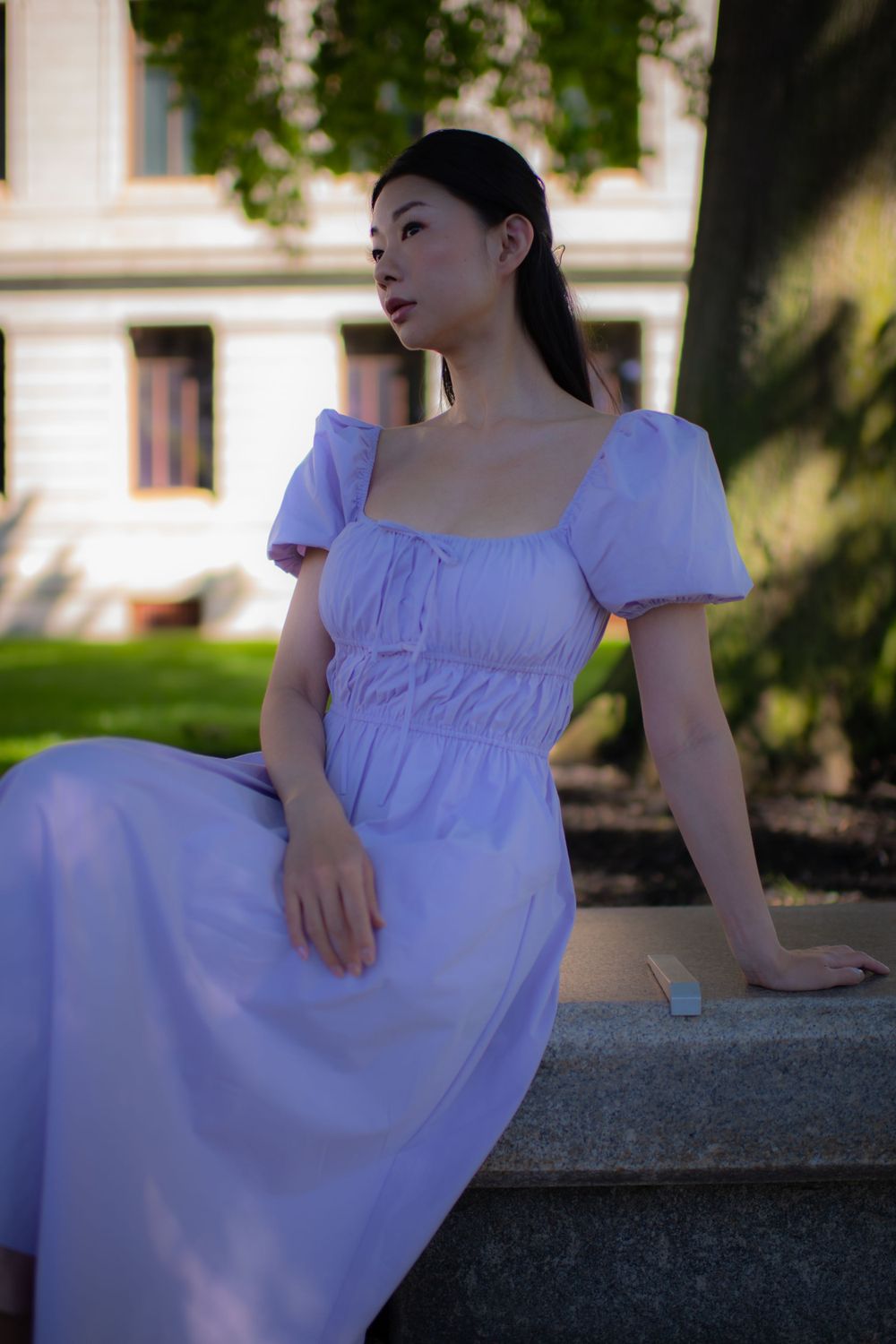 A woman in a white empire waist dress with puff sleeves sits gracefully on stone steps in a garden setting.