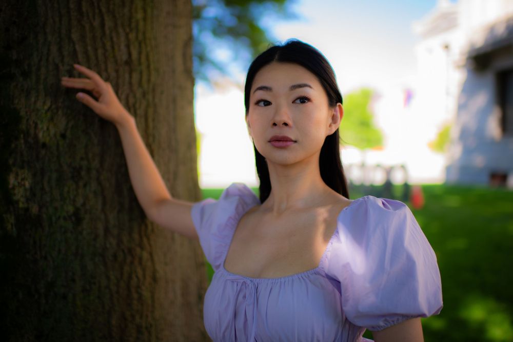 Outdoor portrait featuring a person in a purple dress posing against a tree with soft natural lighting.
