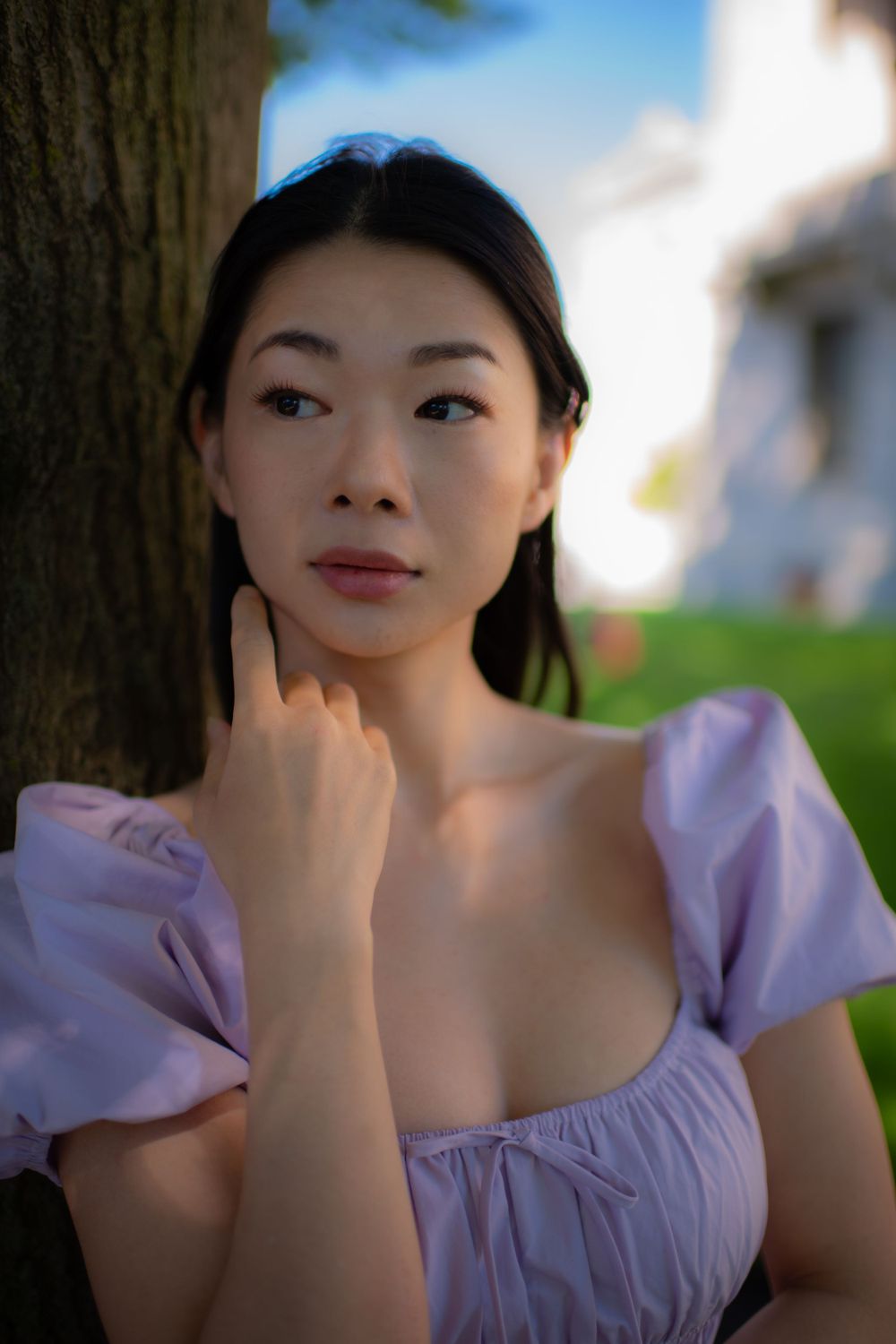 Close-up portrait in soft lighting showing a lavender dress with puff sleeves against a tree trunk background.