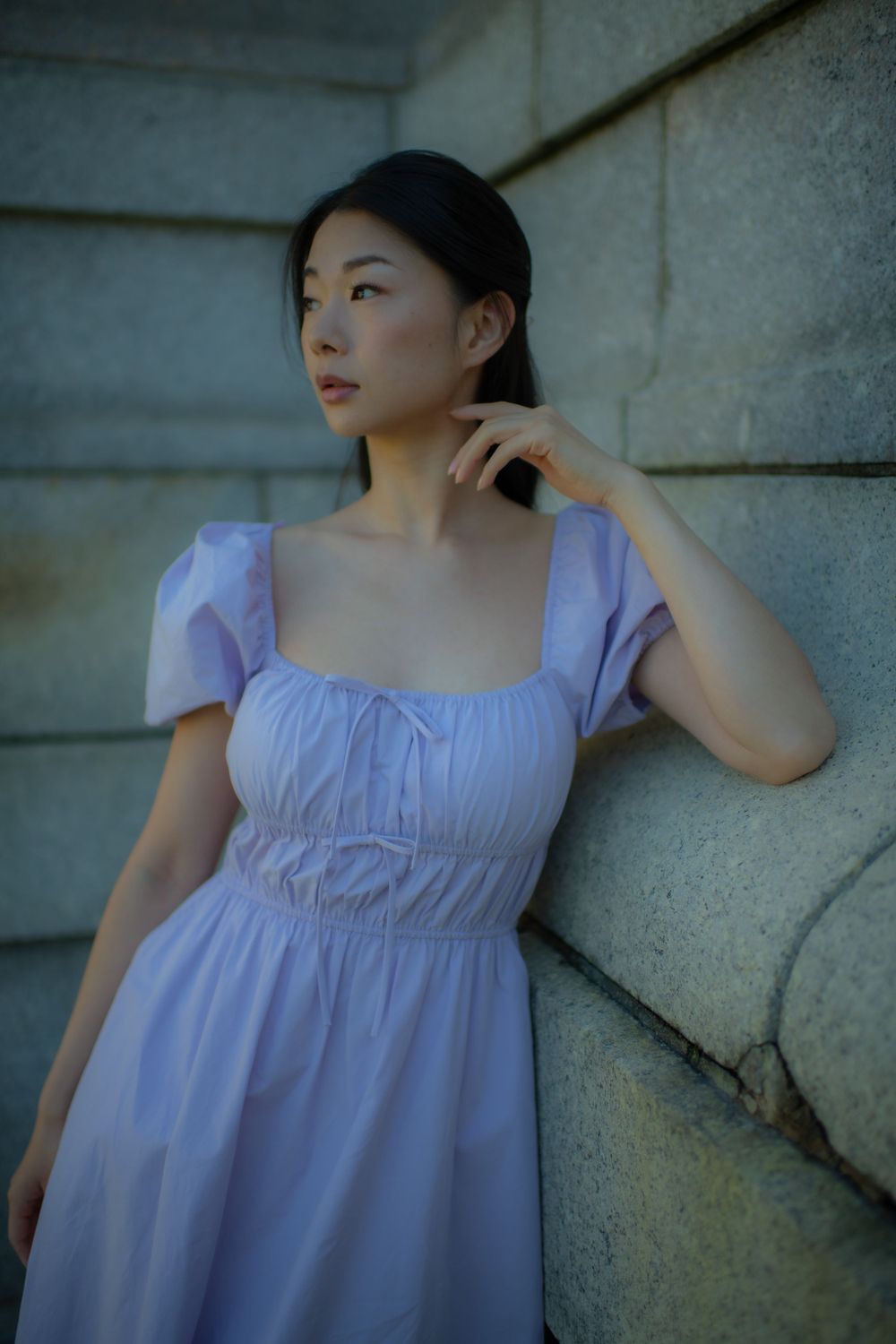 Moody portrait against stone architecture showing a light purple dress with gathered bodice details.
