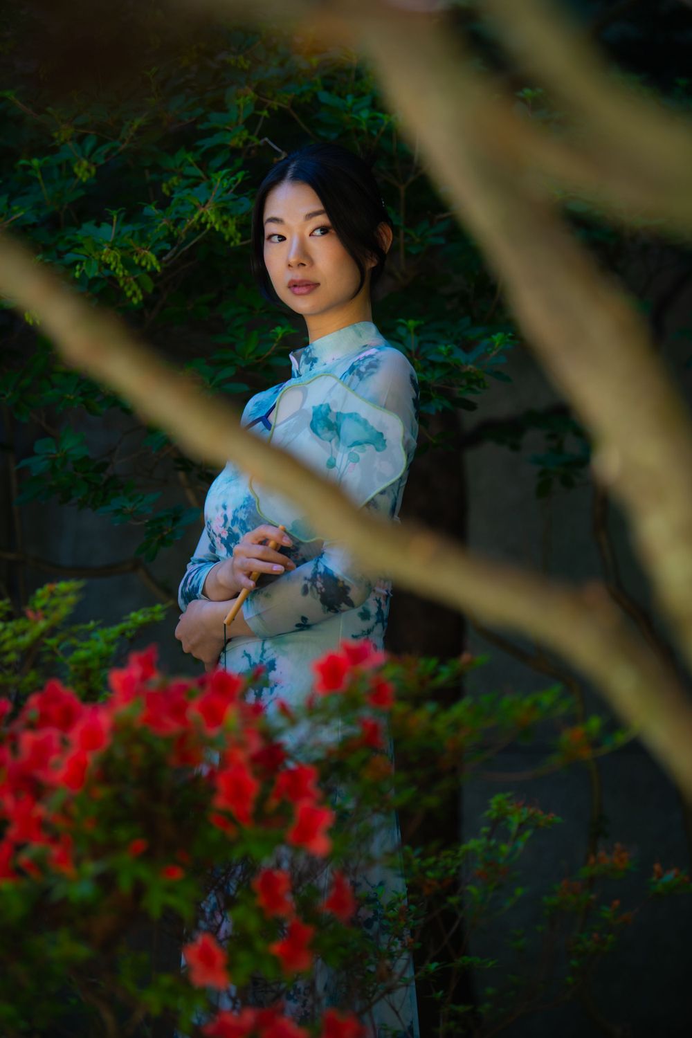 Artistic shot through branches showing a blue floral dress amid red flowers and greenery.