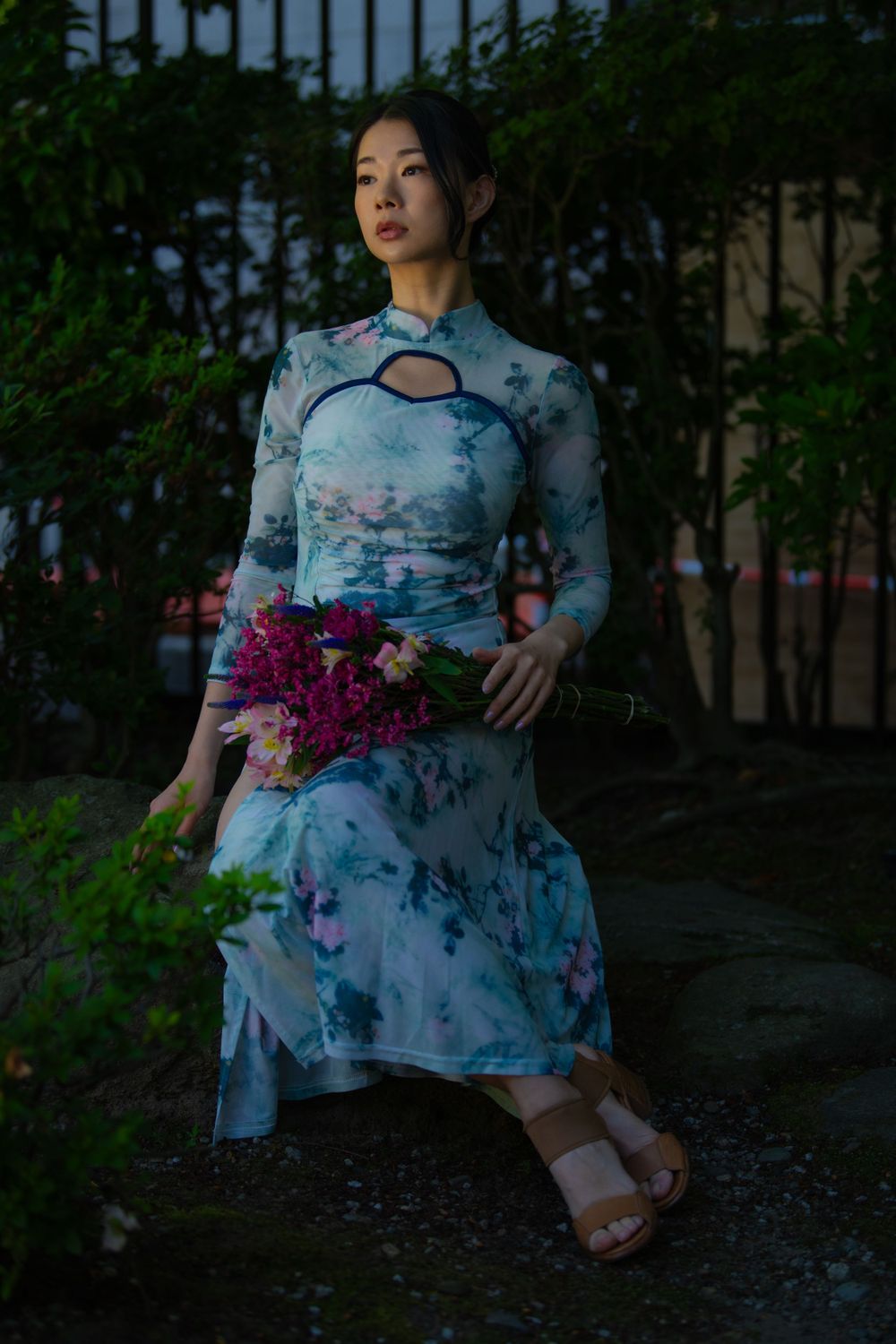 Person wearing blue floral dress poses with flowers in evening garden light.