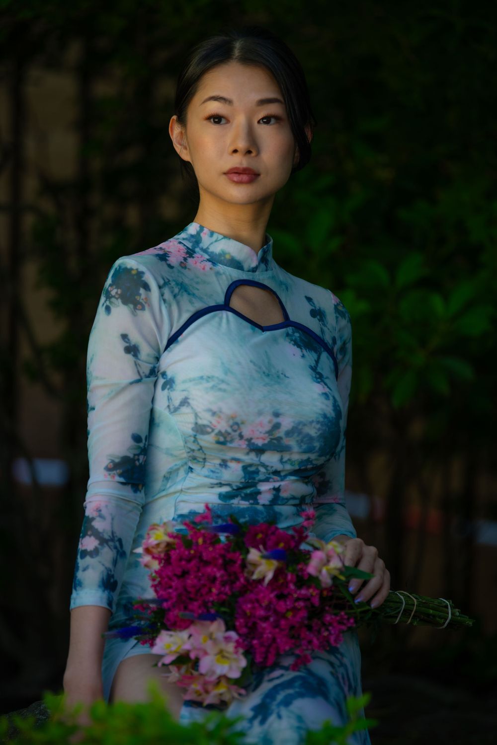 Elegant portrait featuring a blue and white floral qipao dress with pink flower bouquet.