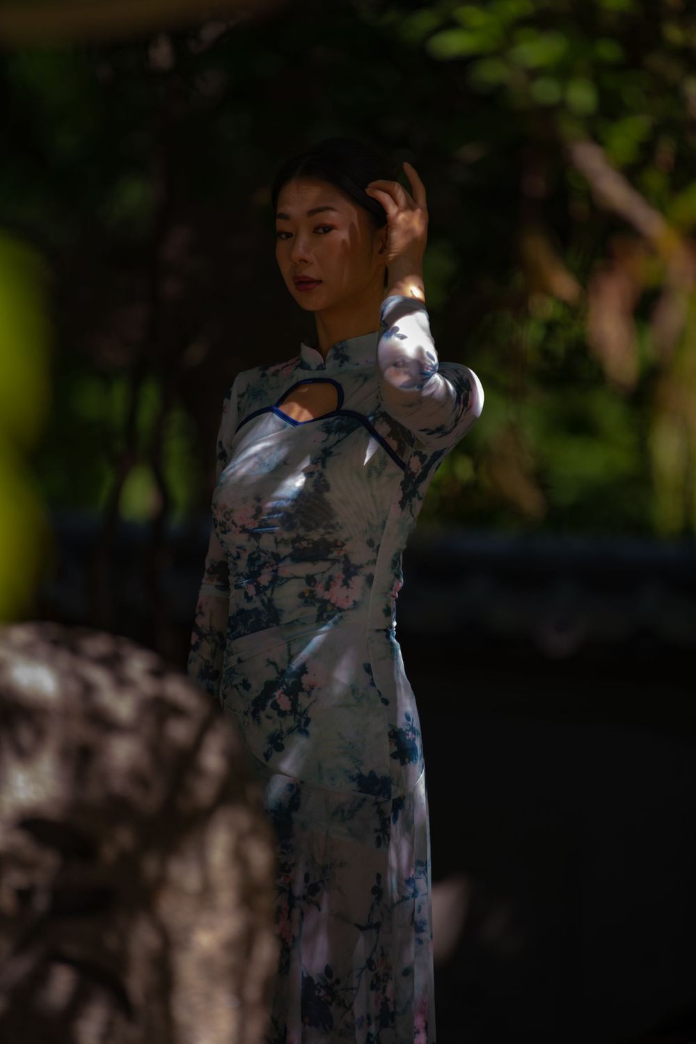 Figure in traditional patterned dress poses in dramatic shadows and natural lighting.