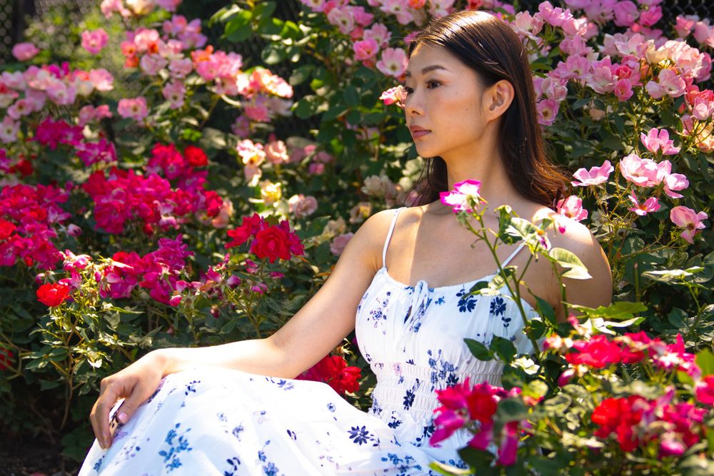 Model in summer dress poses gracefully amid blooming rose garden.
