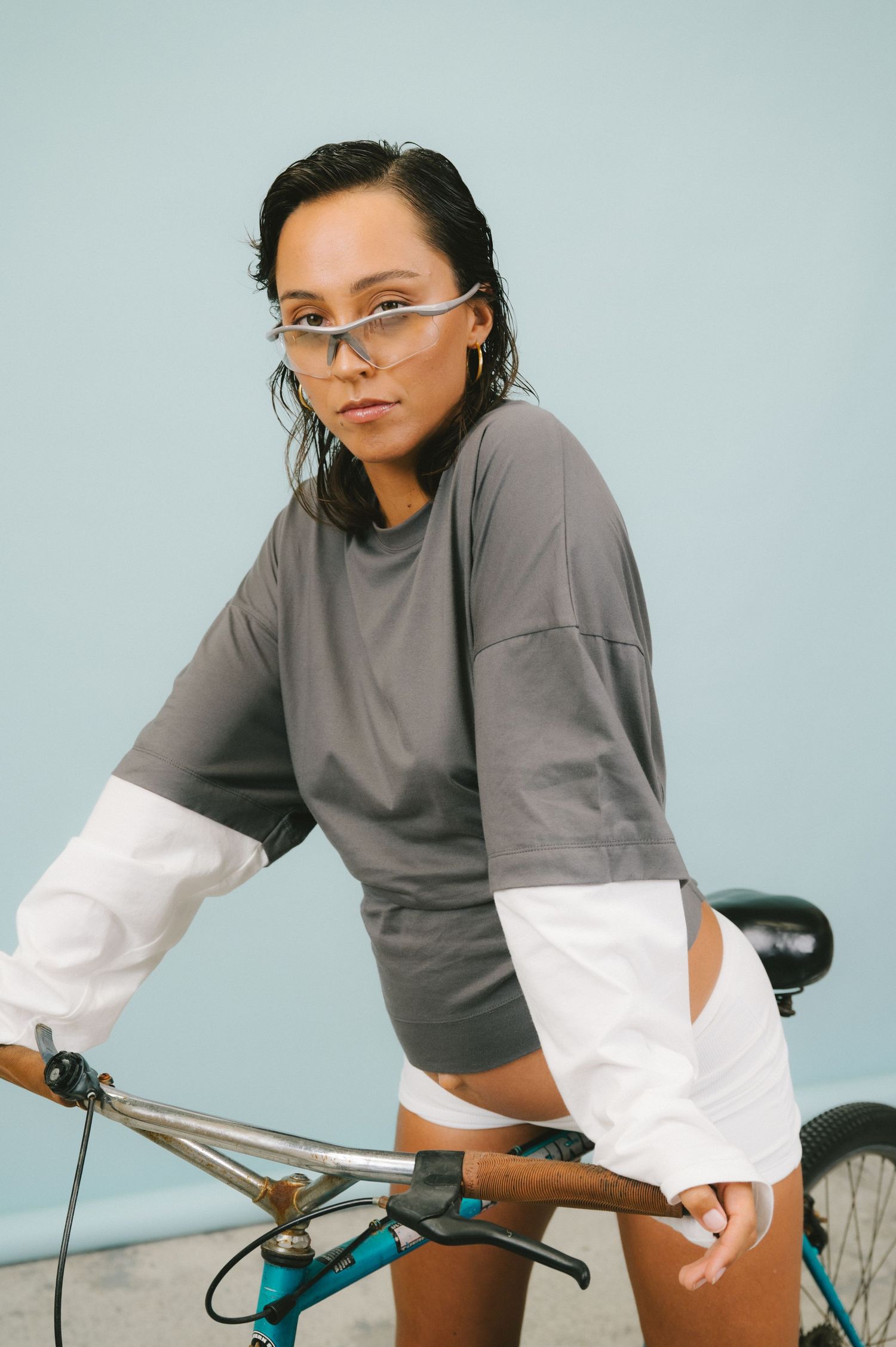 Athletic cyclist in sportswear with futuristic sunglasses poses with bicycle against light blue background.