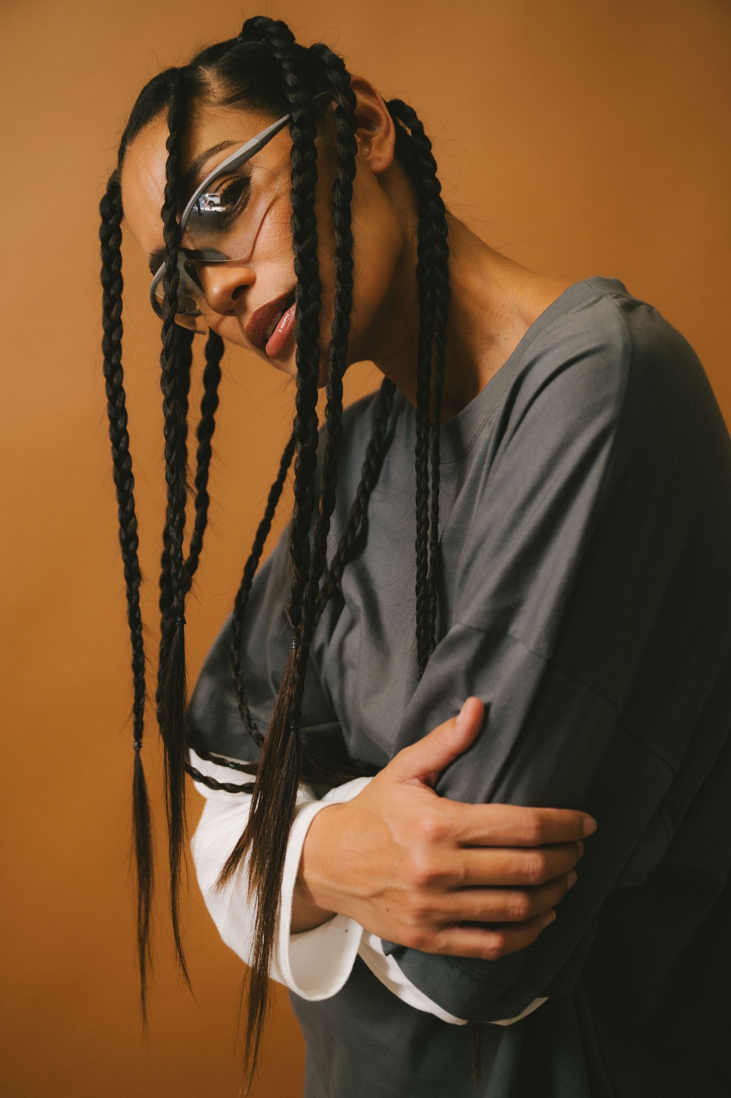 Portrait series showing long braided hair in motion against warm brown backdrop, wearing gray and white clothing.