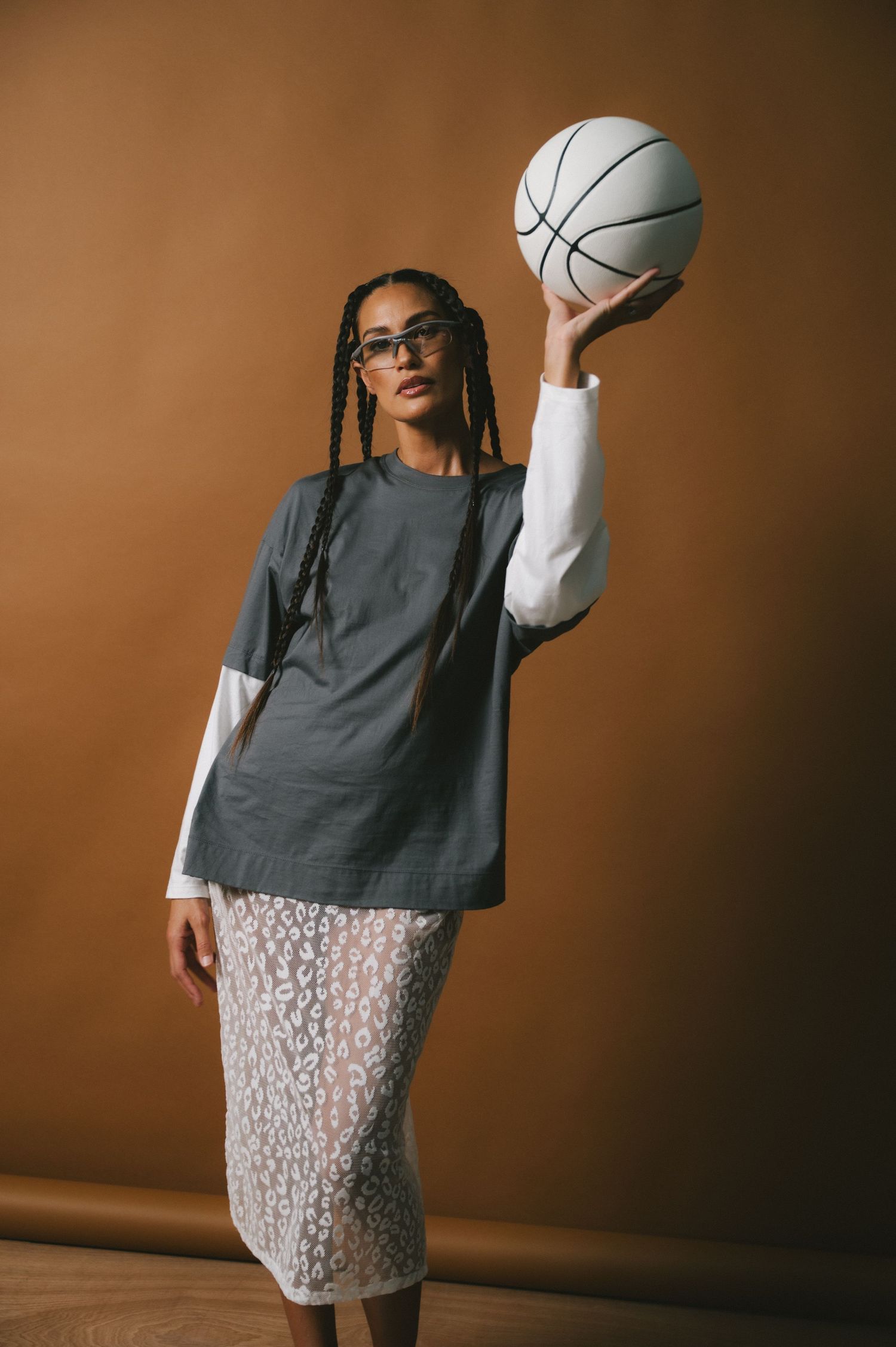 A figure wearing a grey top and patterned skirt strikes dynamic poses with a ball against a brown backdrop in a photo series.