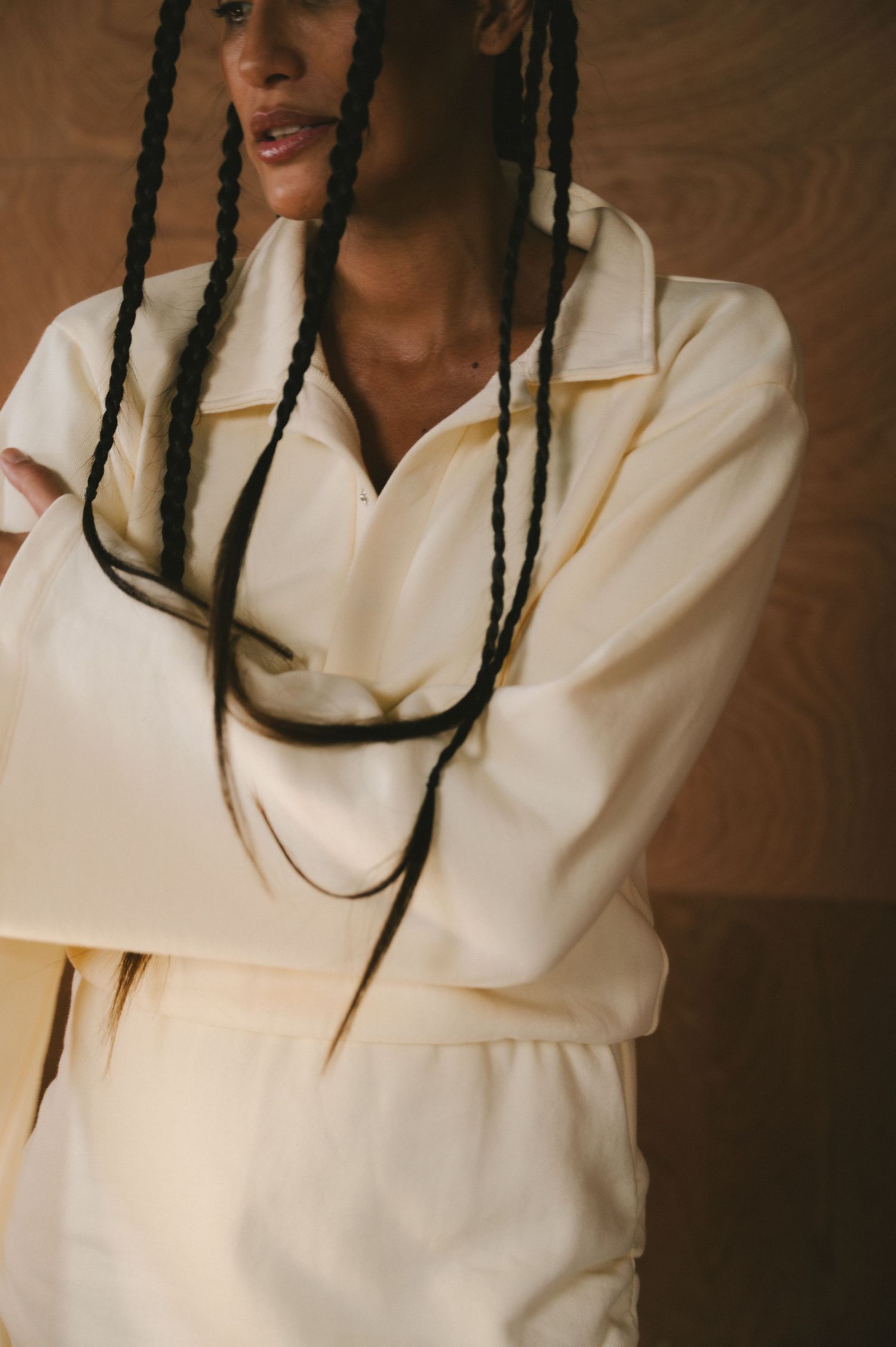 A person wearing a crisp white sweater and long dark braids is shown in a series of five close-up poses against a brown backdrop.