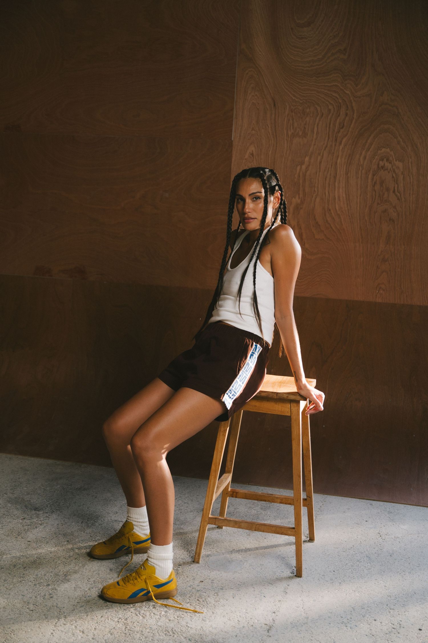 Person wearing yellow boots and white socks sits on wooden chair against textured brown wall.