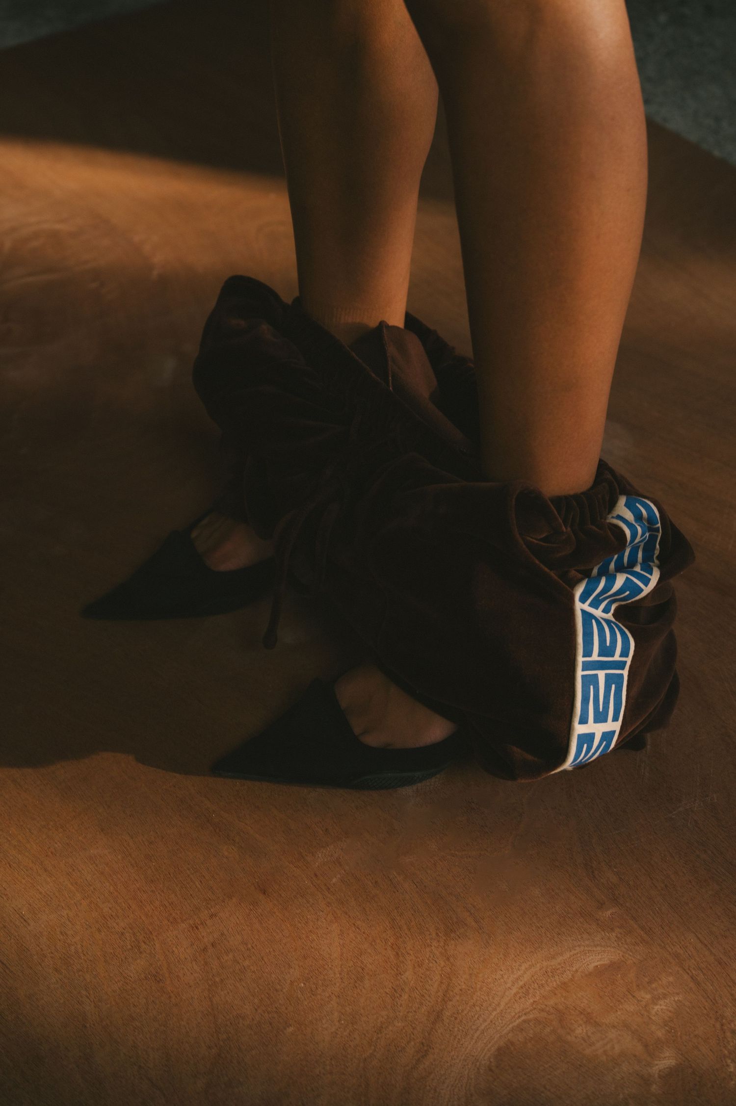 Close-up view of black slippers with glowing blue neon details on a dark wooden floor.