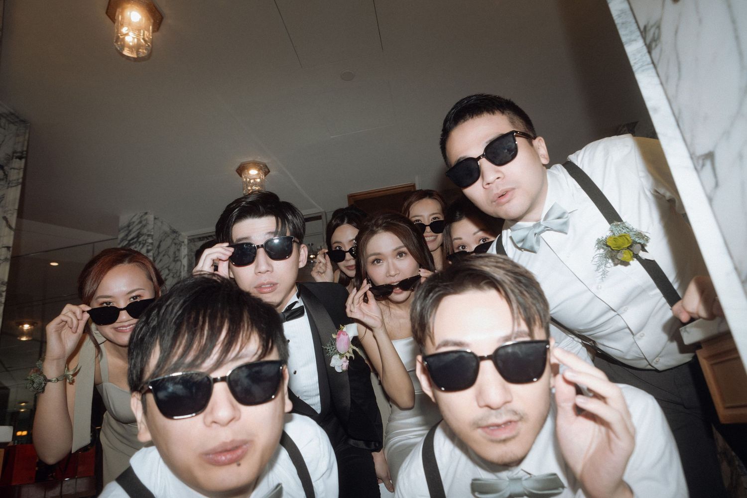 A group wearing sunglasses and formal attire poses together for a fun wedding party photo.