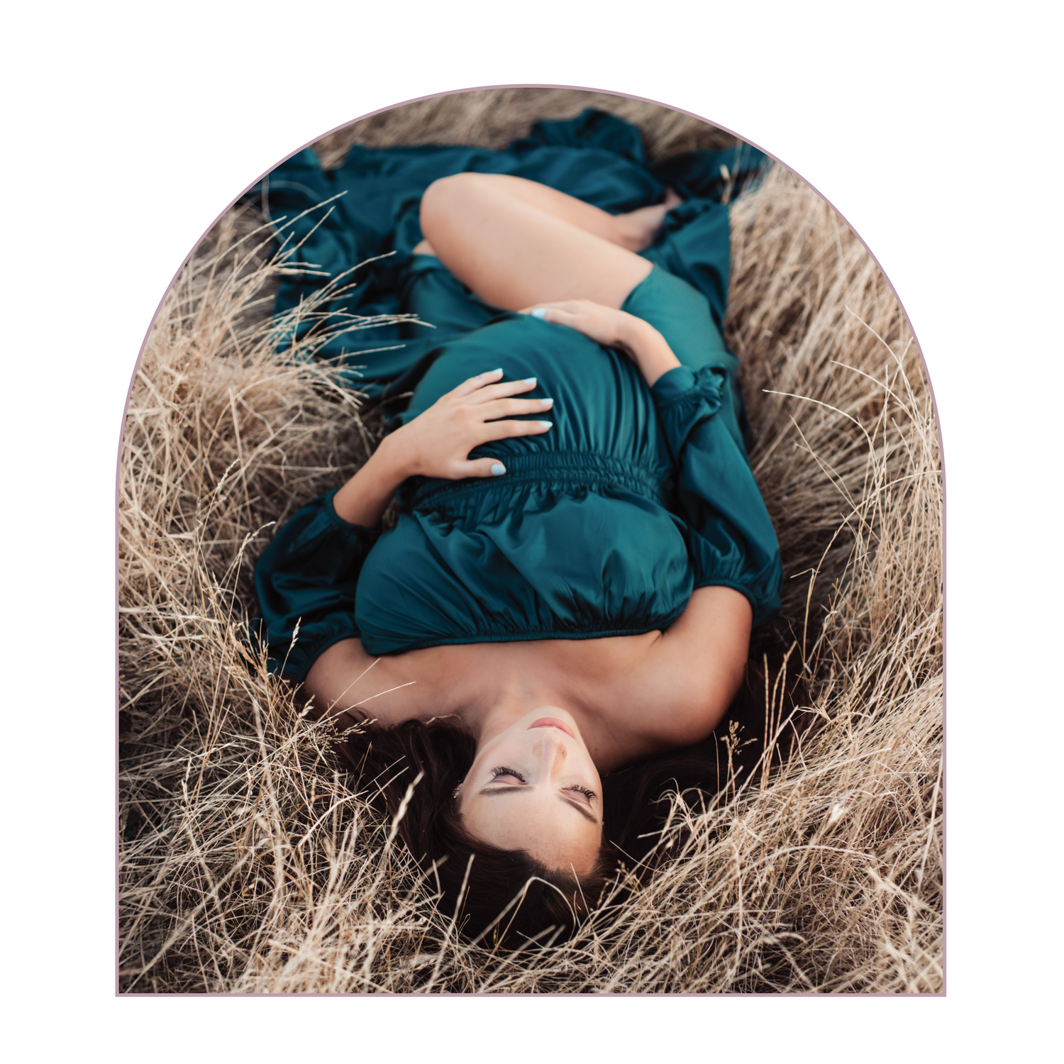 Beautiful maternity photo of woman in teal dress laying in golden grass field.