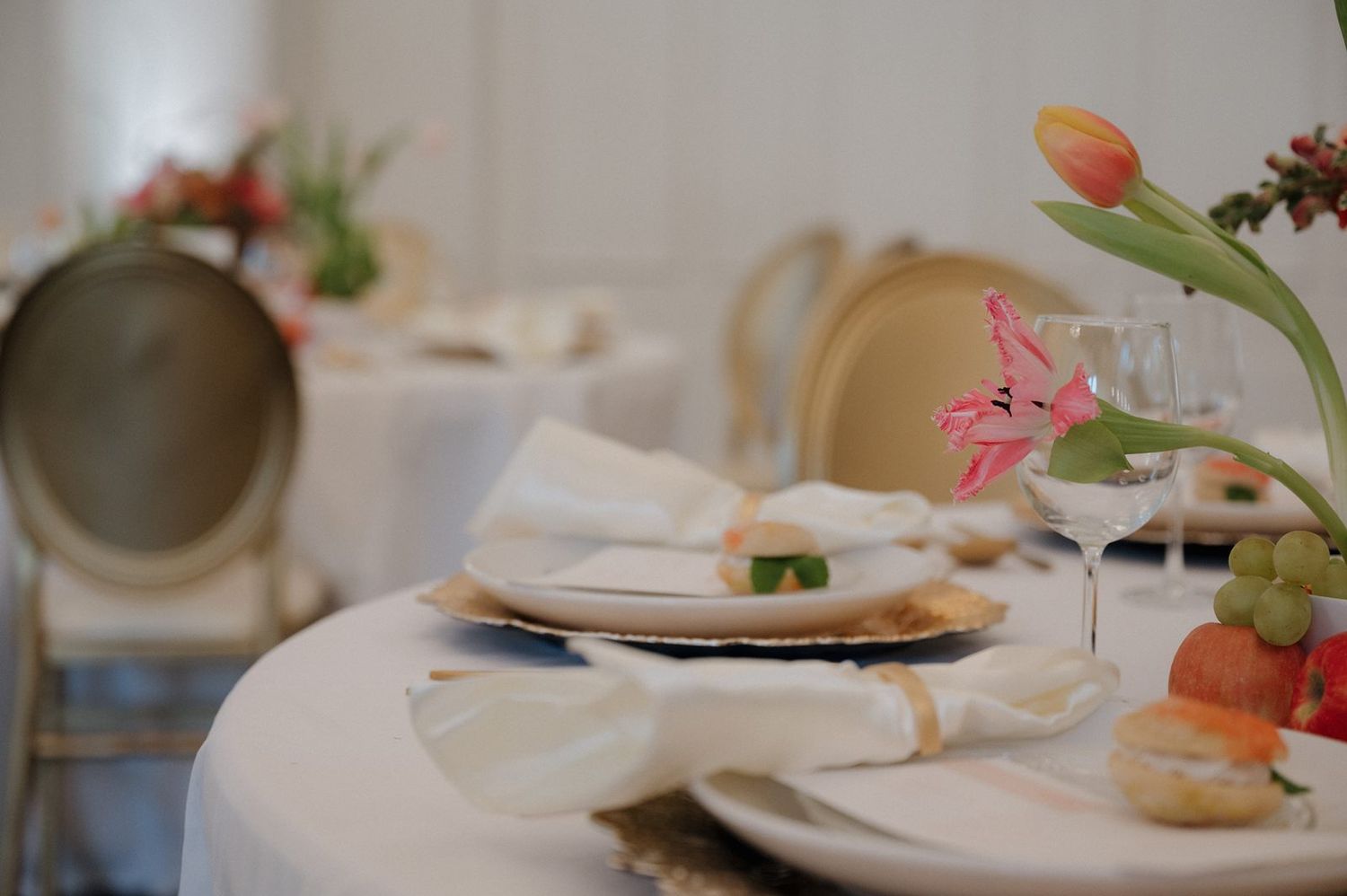 Elegant table setting with pink tulips and white plates in a soft focus restaurant setting with natural lighting.