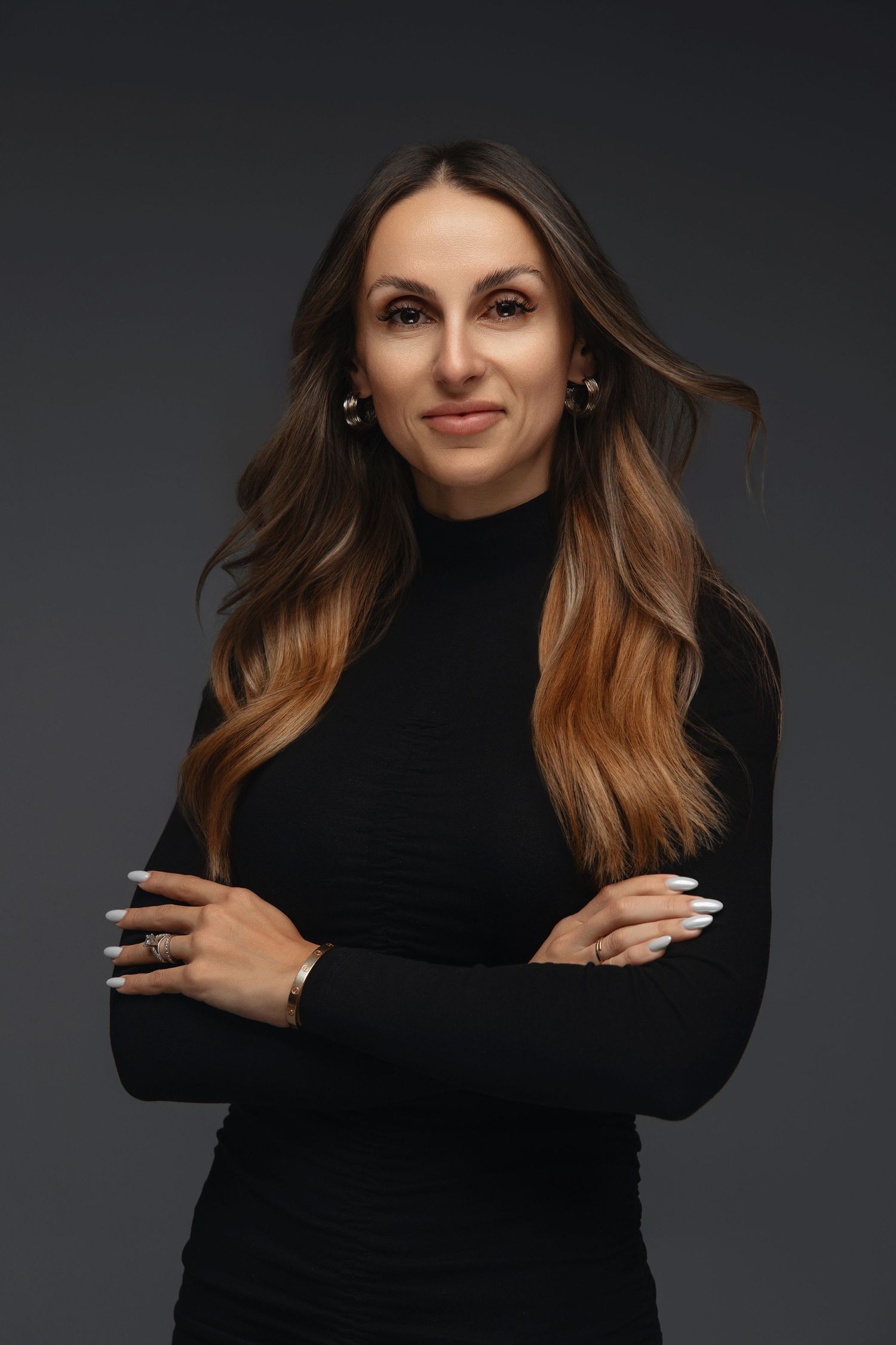 Professional studio portrait of woman in black turtleneck with long wavy hair against dark background.