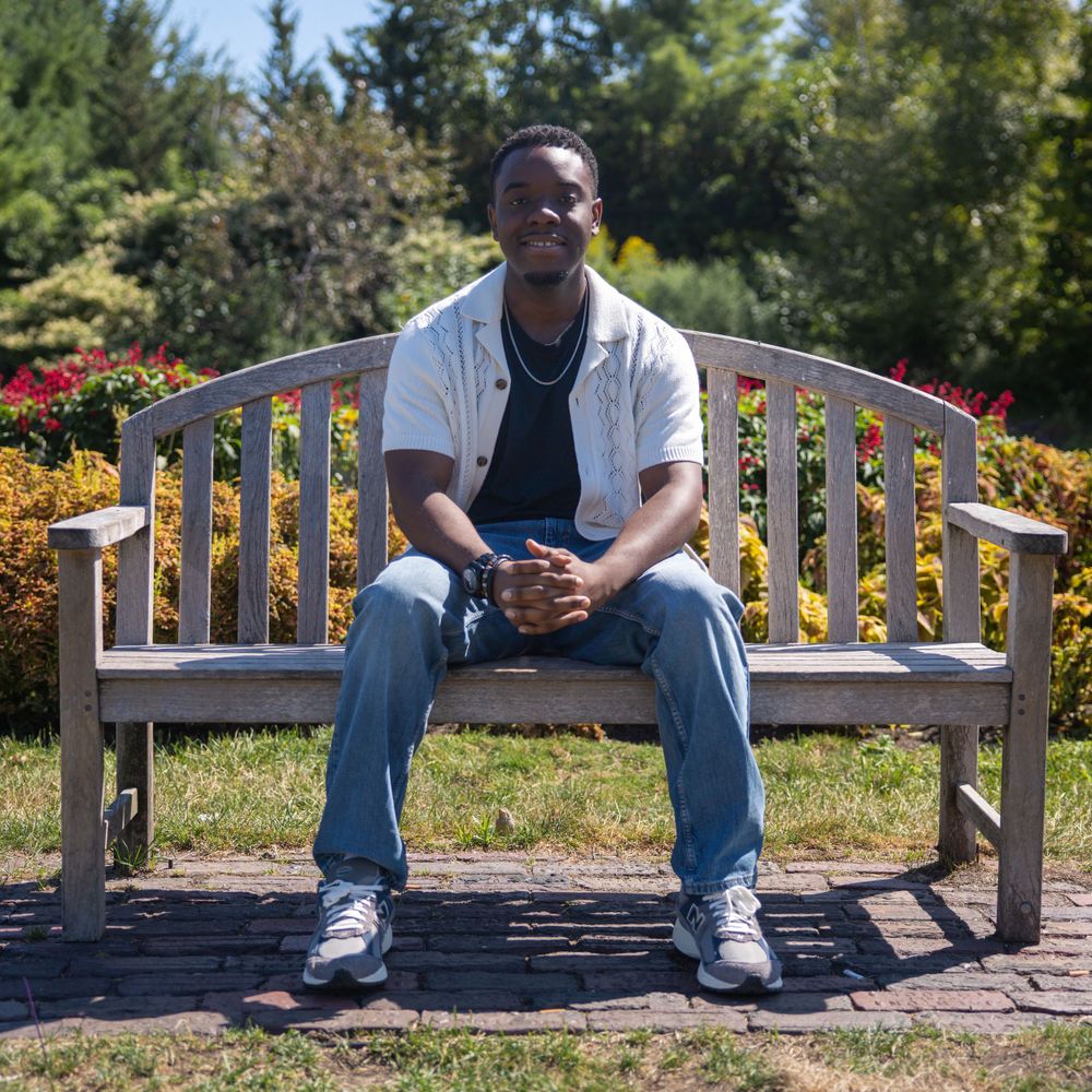 Person relaxing on a wooden bench surrounded by blooming flowers and green foliage.