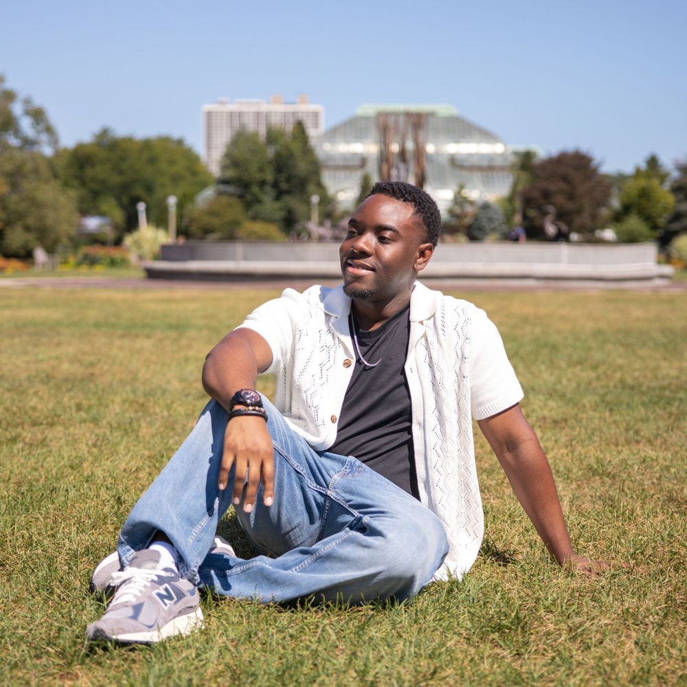 Person lounging on grass in a casual pose with institutional buildings in the background.