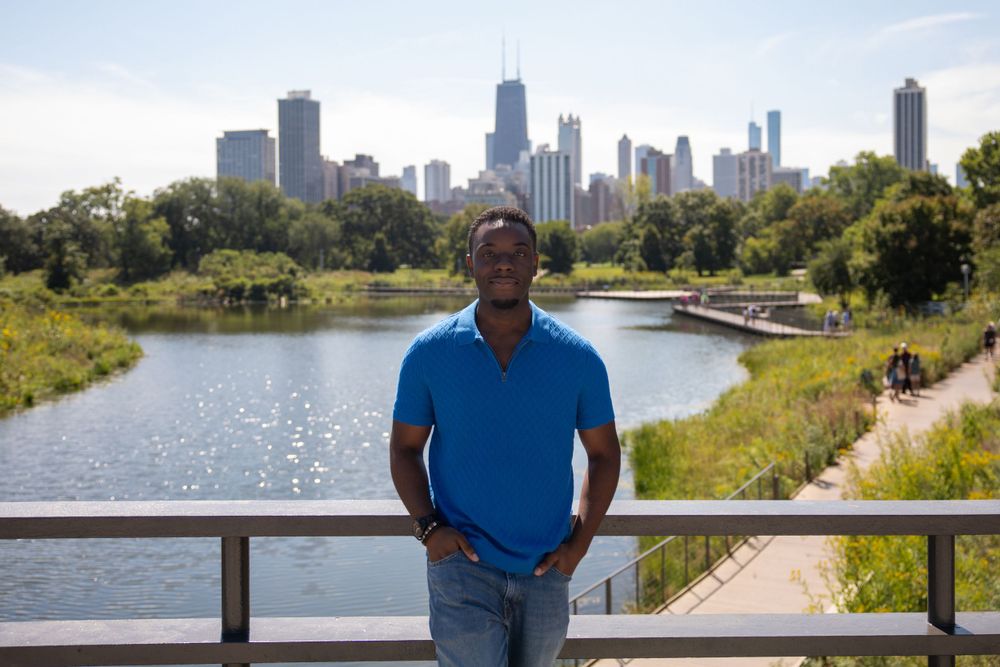 Urban landscape photo with Chicago's skyline visible across a lake with a person standing by a railing.