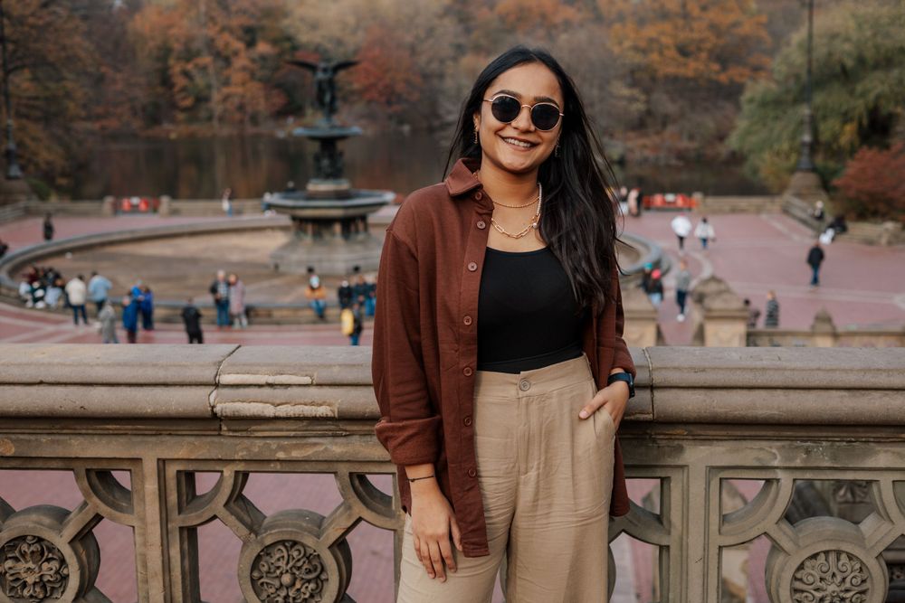 A stylish outfit featuring brown jacket and beige pants against an autumn park backdrop.