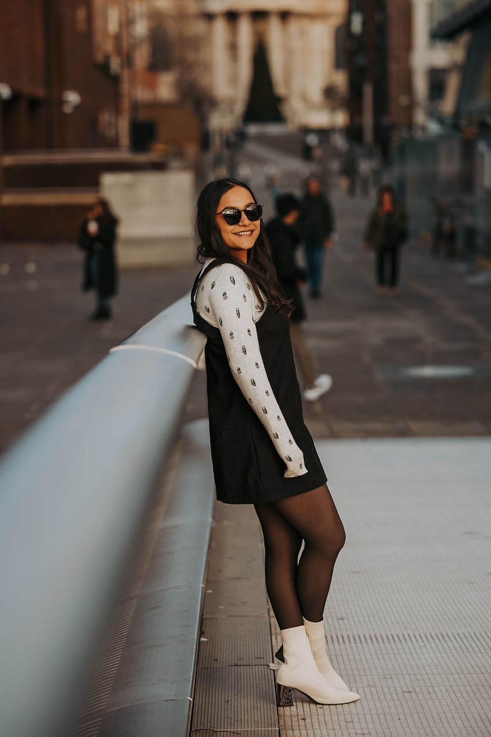 Stylish winter outfit featuring black dress, white sleeves and boots against urban backdrop.