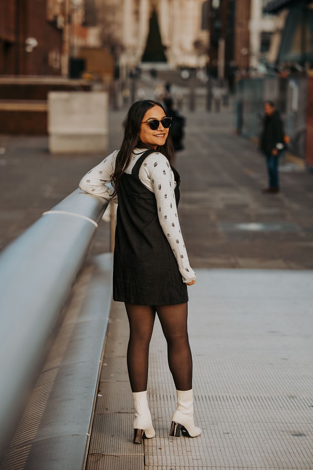 Street style fashion pose featuring black dress with white polka dot sleeves and white boots.
