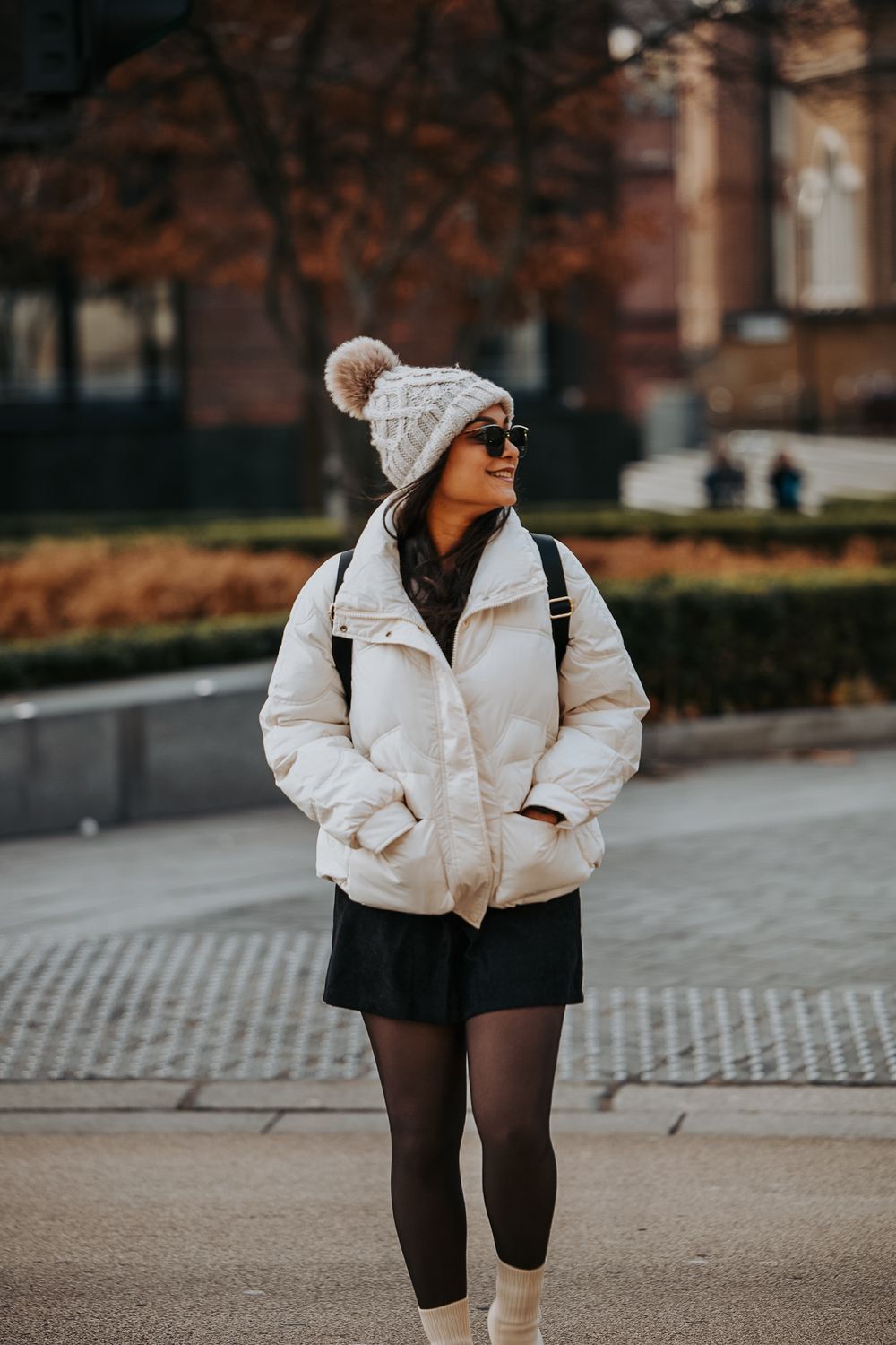 Winter fashion look with puffer jacket, knit beanie and sunglasses in urban setting.
