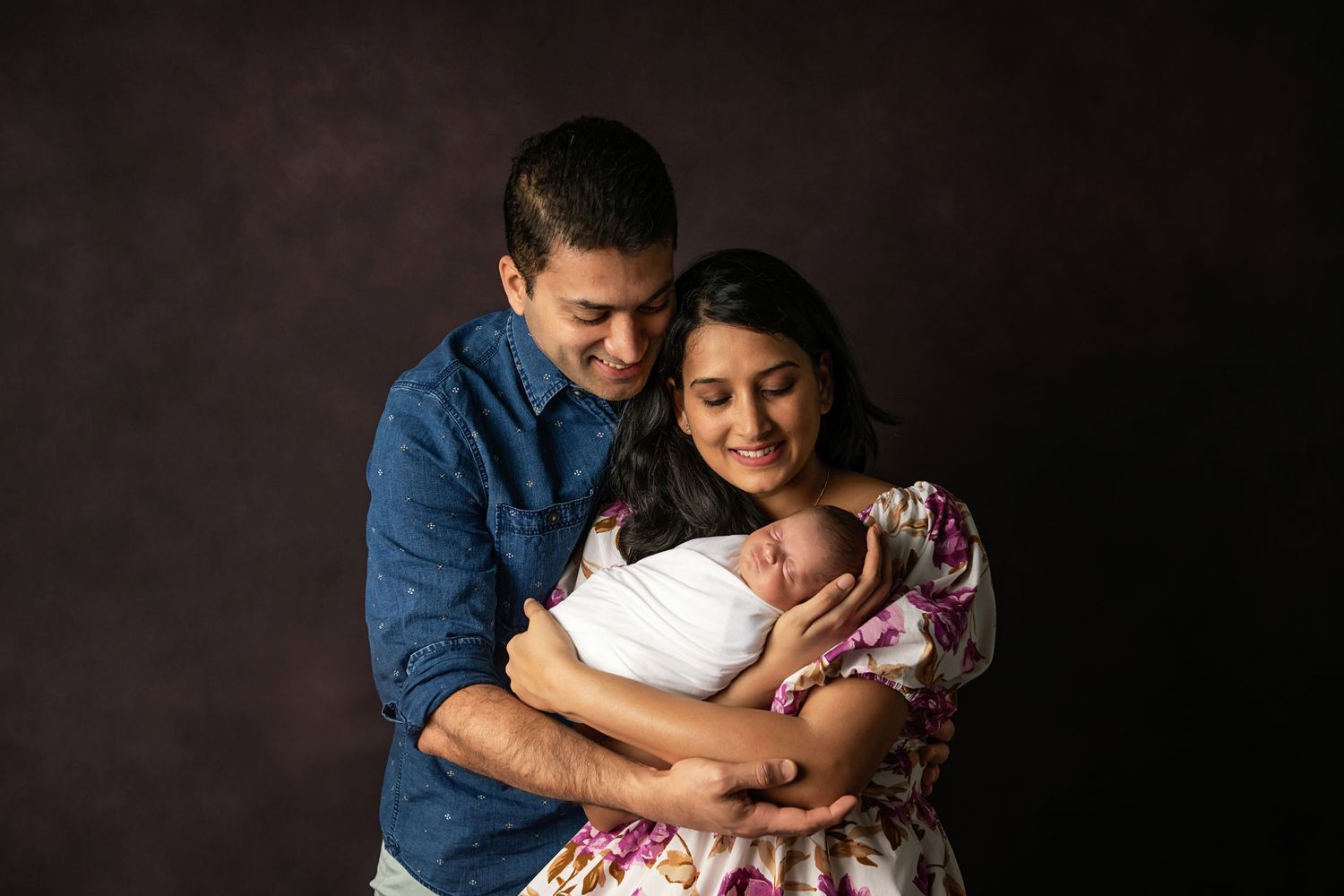 Family shares intimate moment with newborn baby against dark studio background.