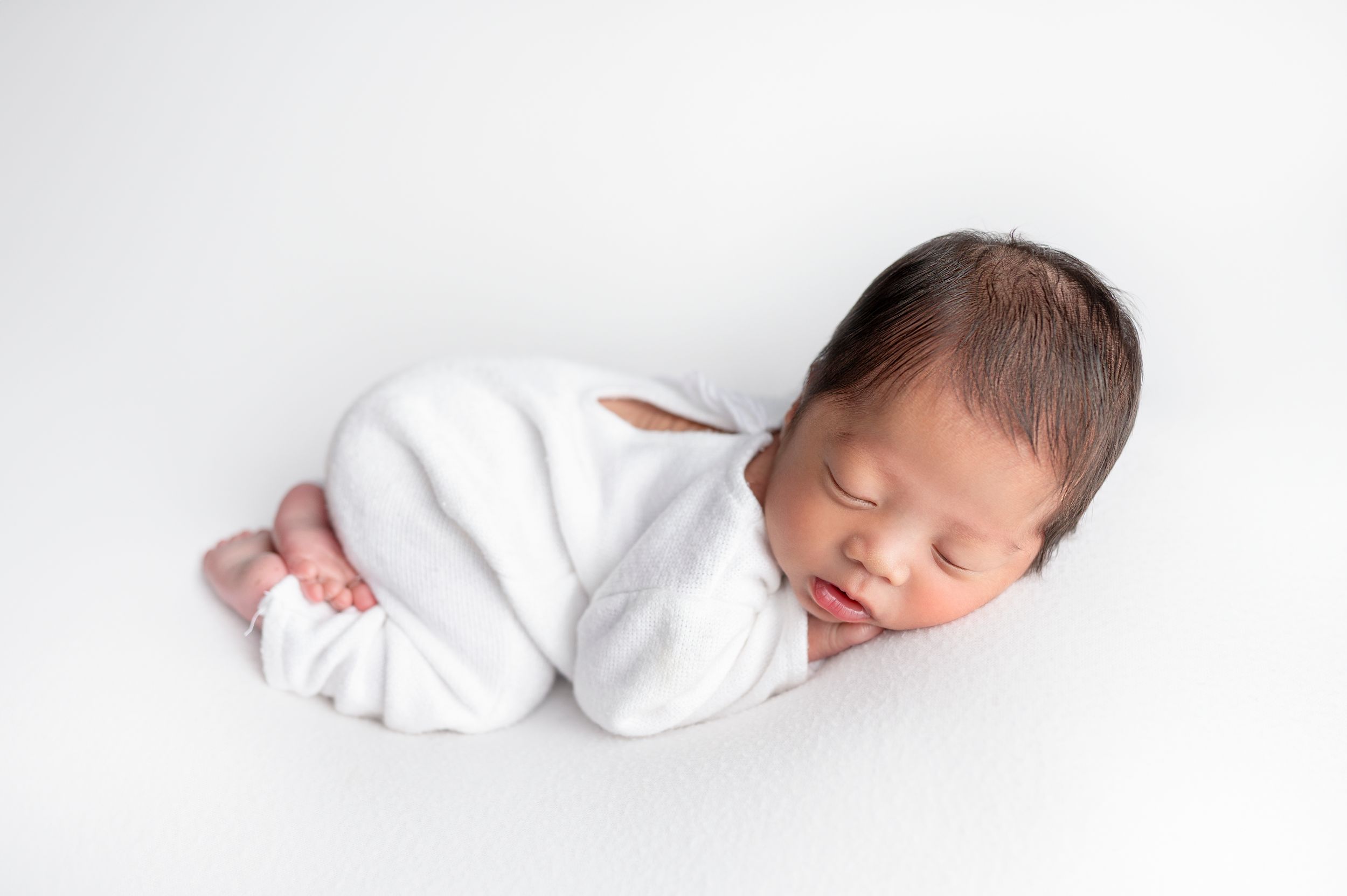 Minimalist newborn photography in Brooklyn, NY, with a sleeping baby in soft white tones for a timeless, pure look.